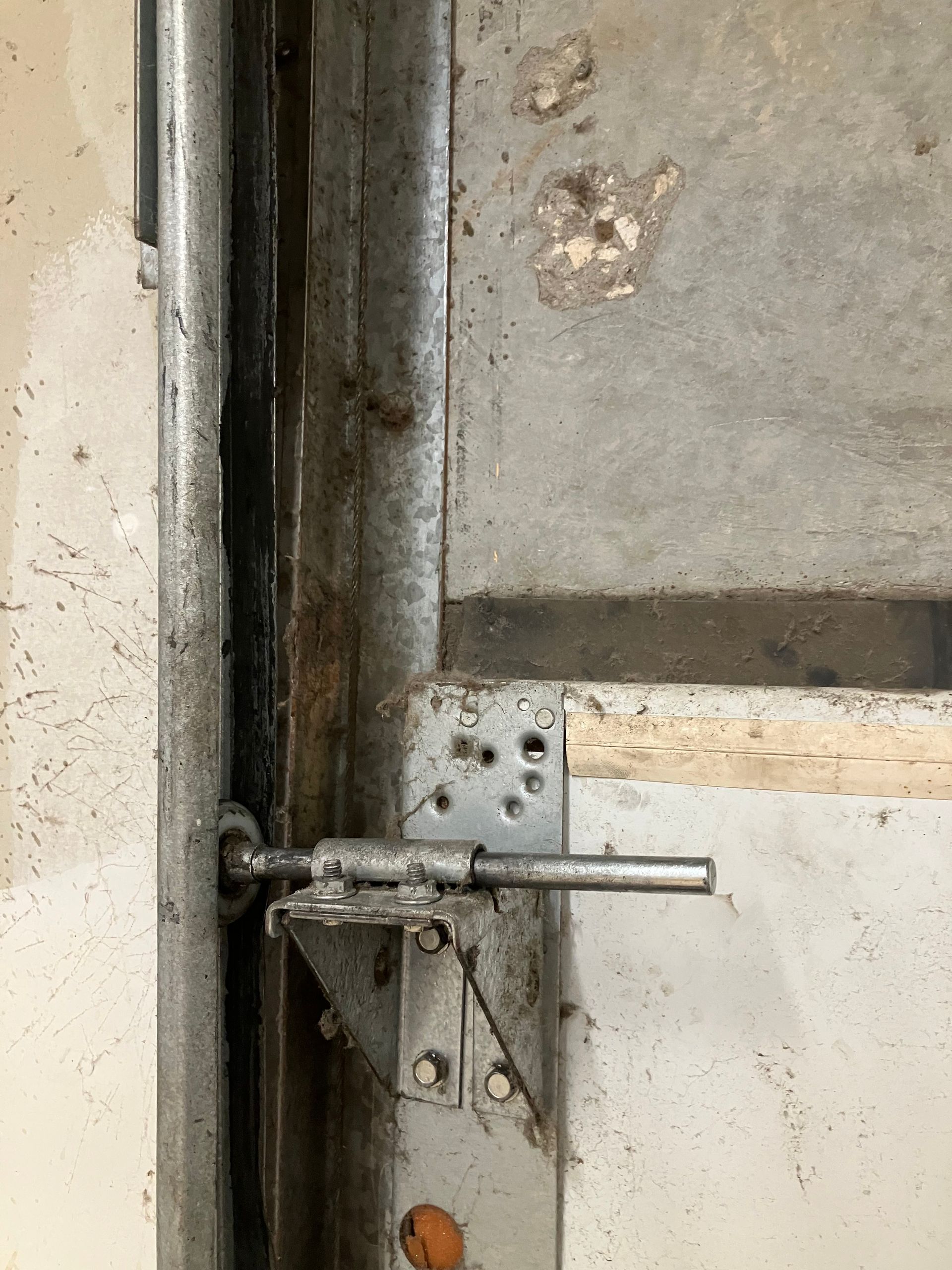 Rusty metal latch on a weathered door with a gray wall background
