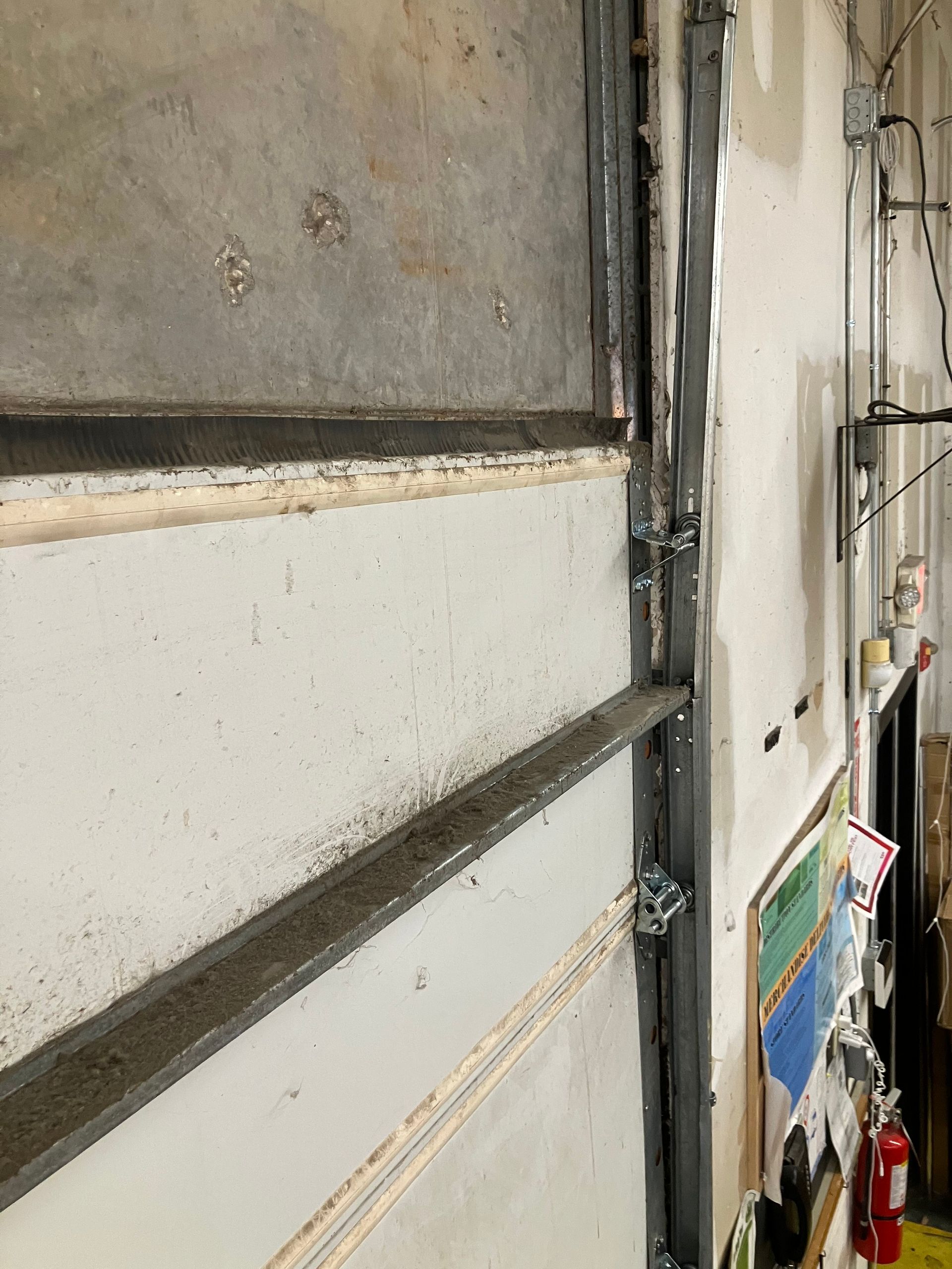 Close-up of a metal garage door track and weathered wall in a narrow indoor space