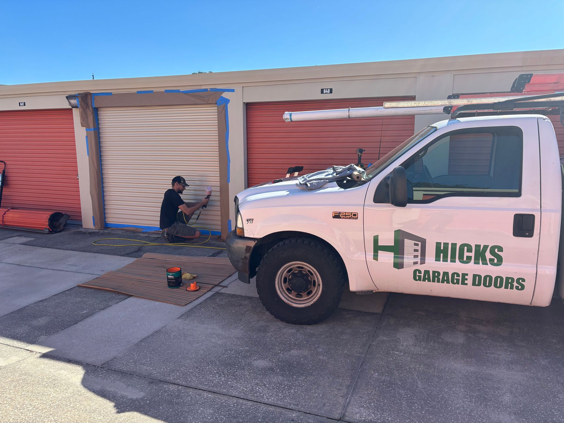 Worker at a storage unit doorway beside a white Hicks Garage Doors truck.