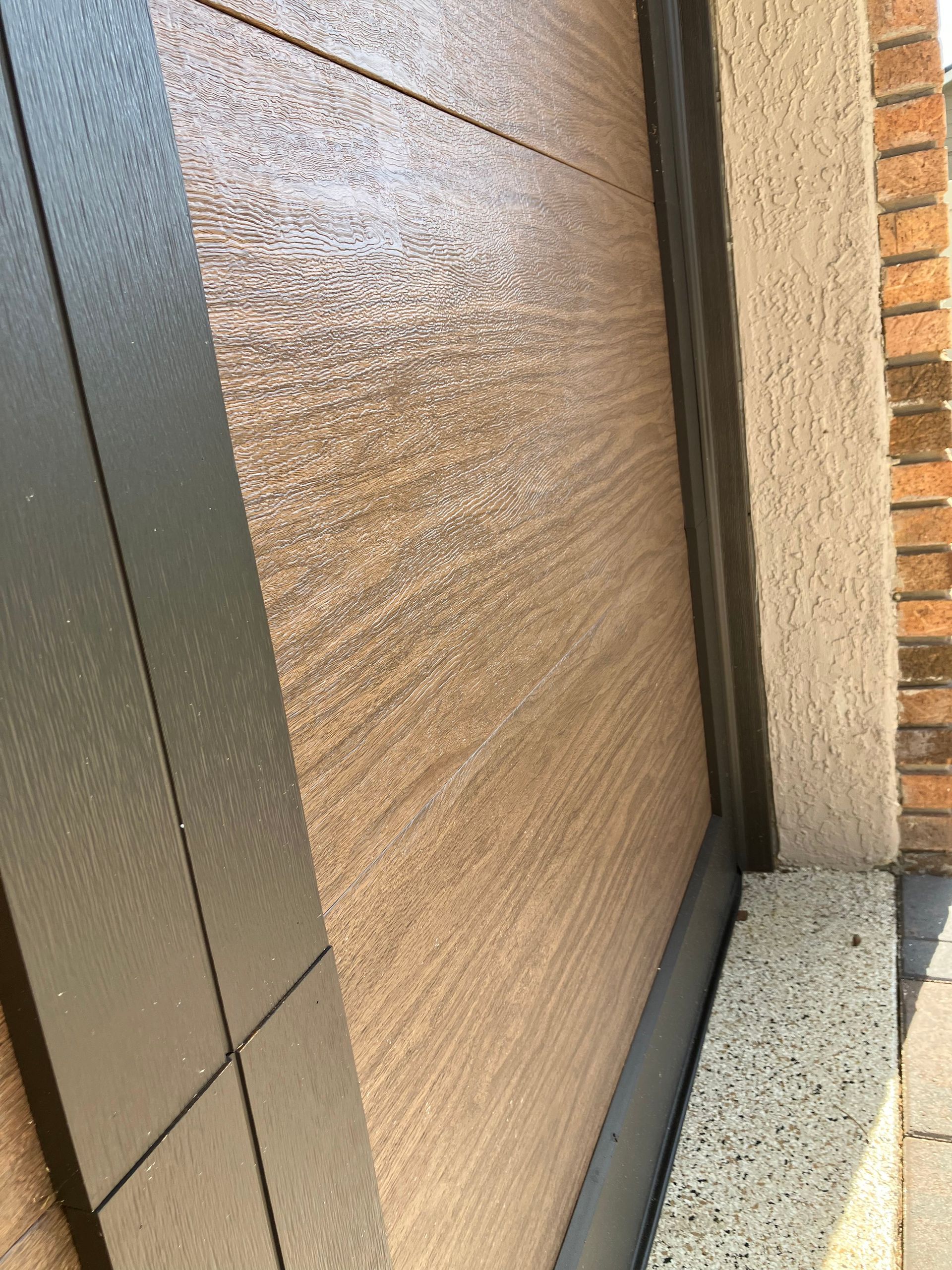 Close-up of a textured tan wall beside a dark doorframe and brick exterior corner.