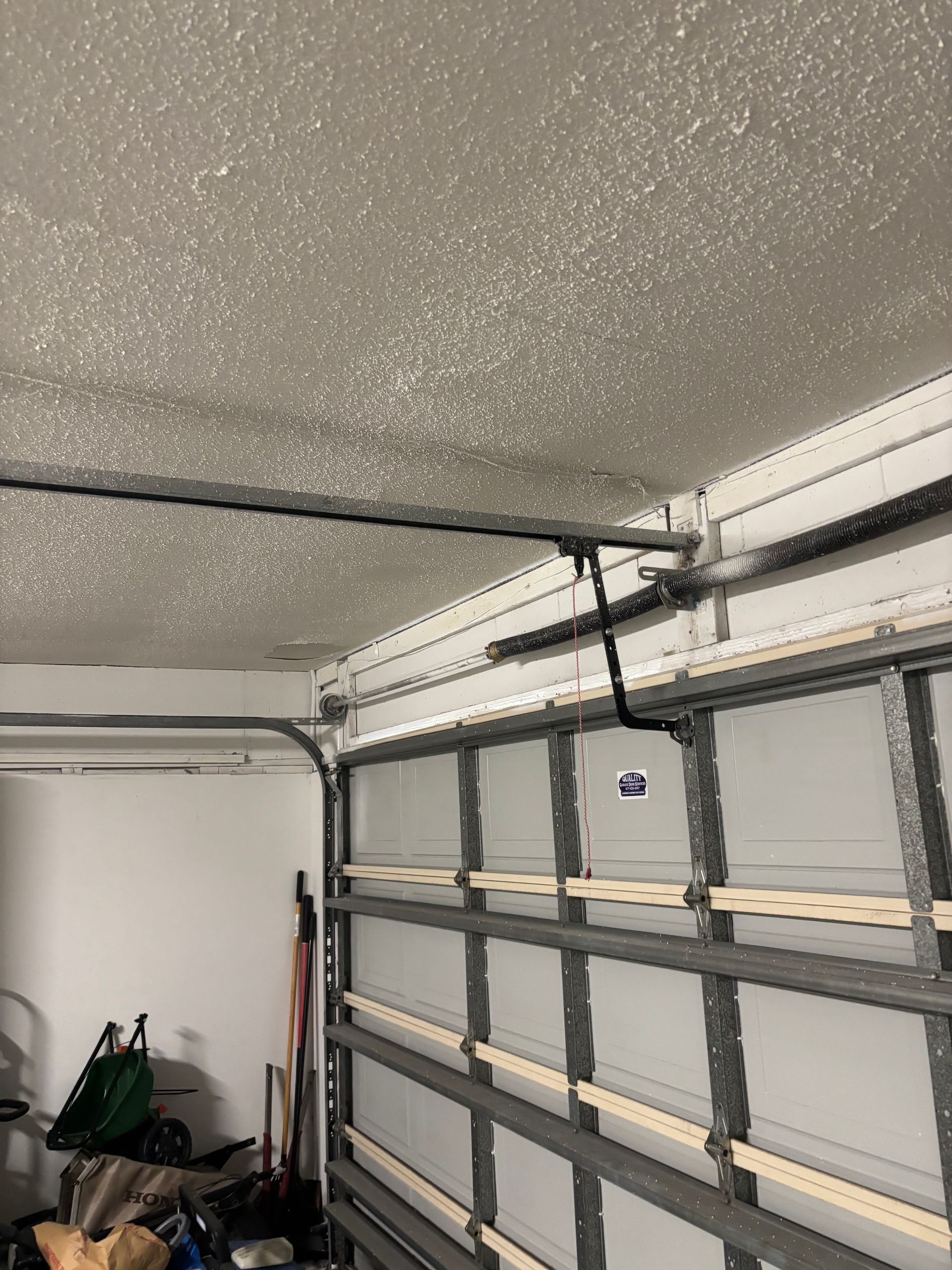 Garage interior with a sectional garage door, ceiling opener rails, and tools stored along the wall.