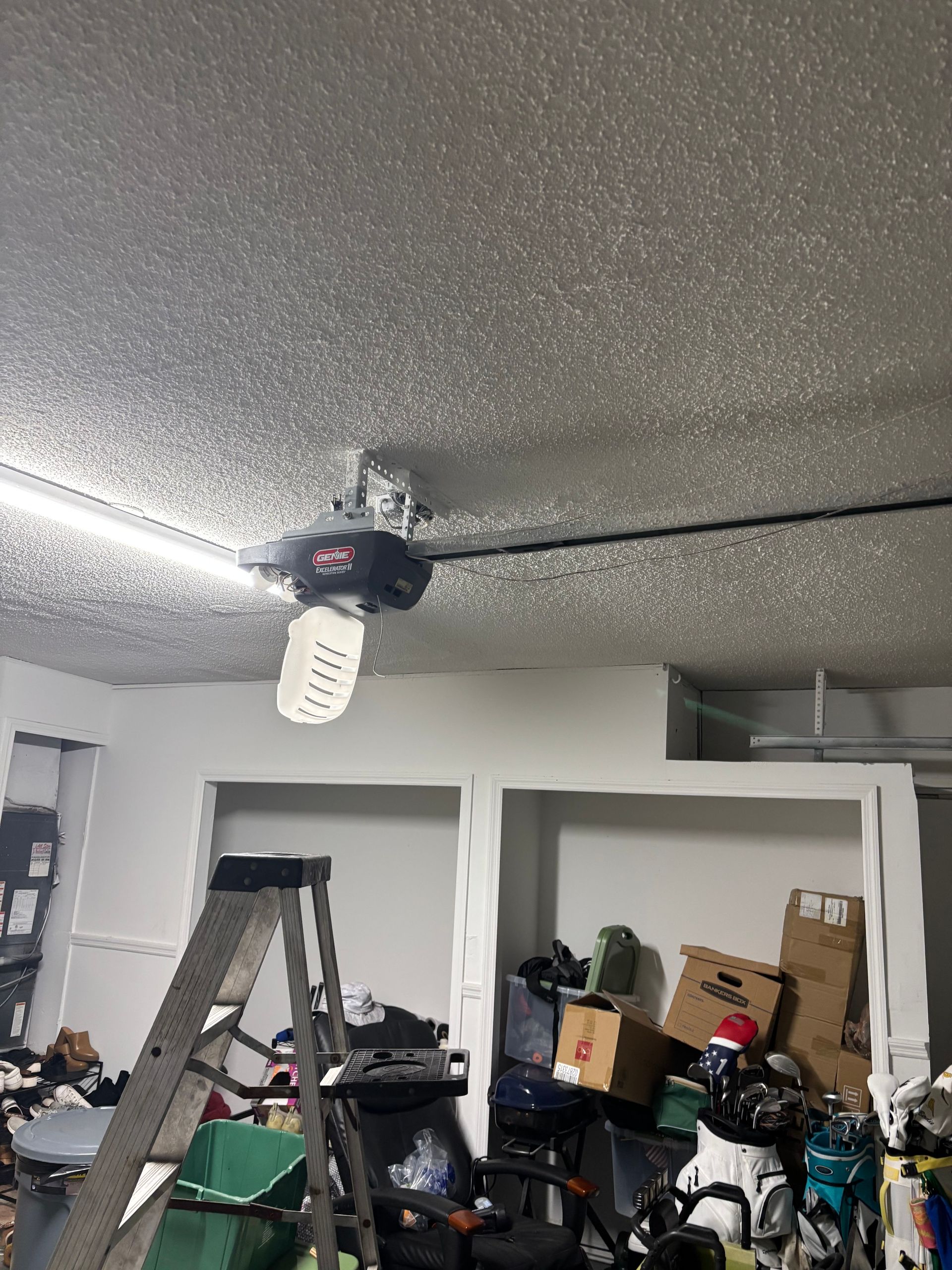 Garage ceiling with a garage door opener, ladder, and storage shelves in a cluttered workspace