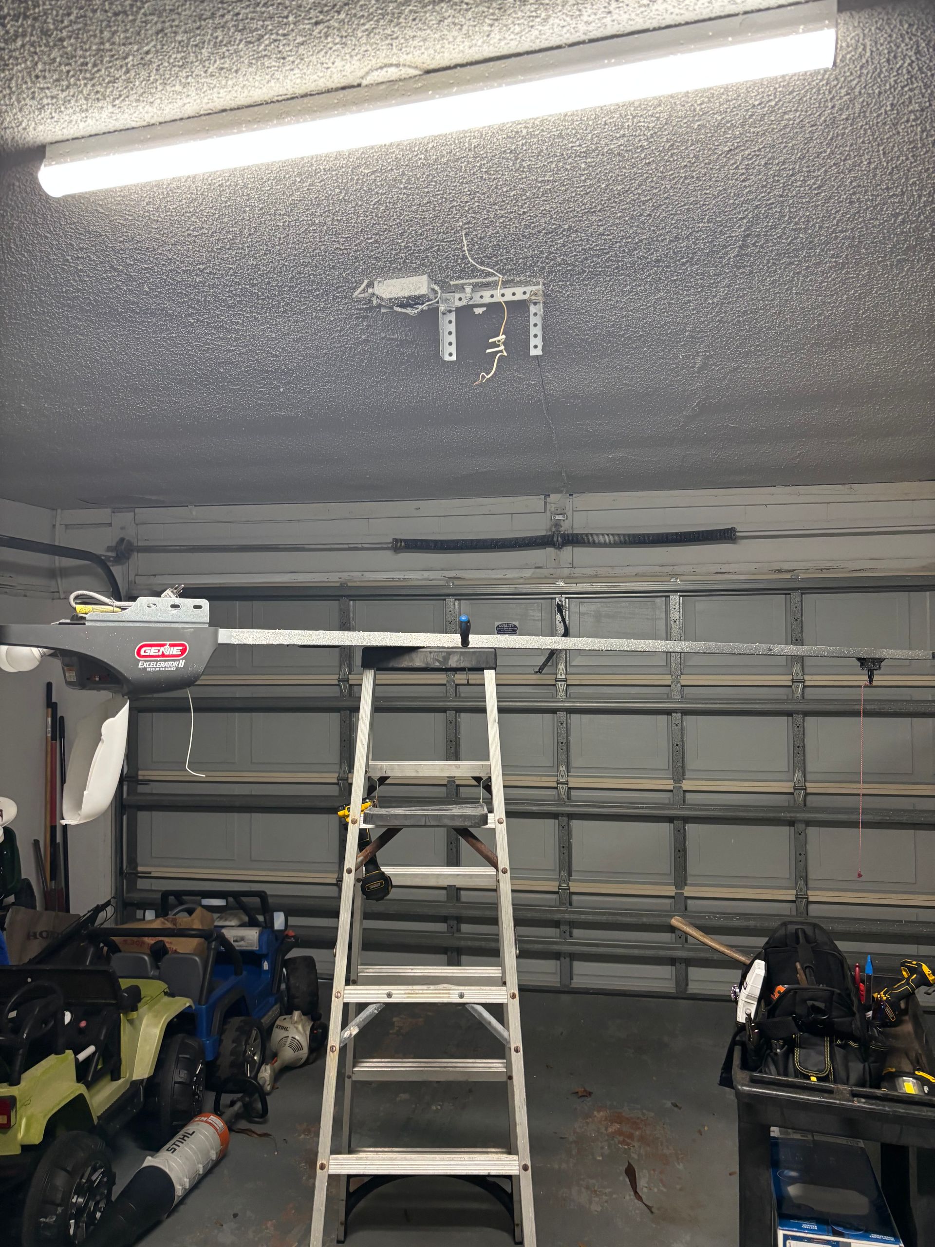 Garage interior with open ceiling, ladder centered, and tools/snowblowers along the walls.