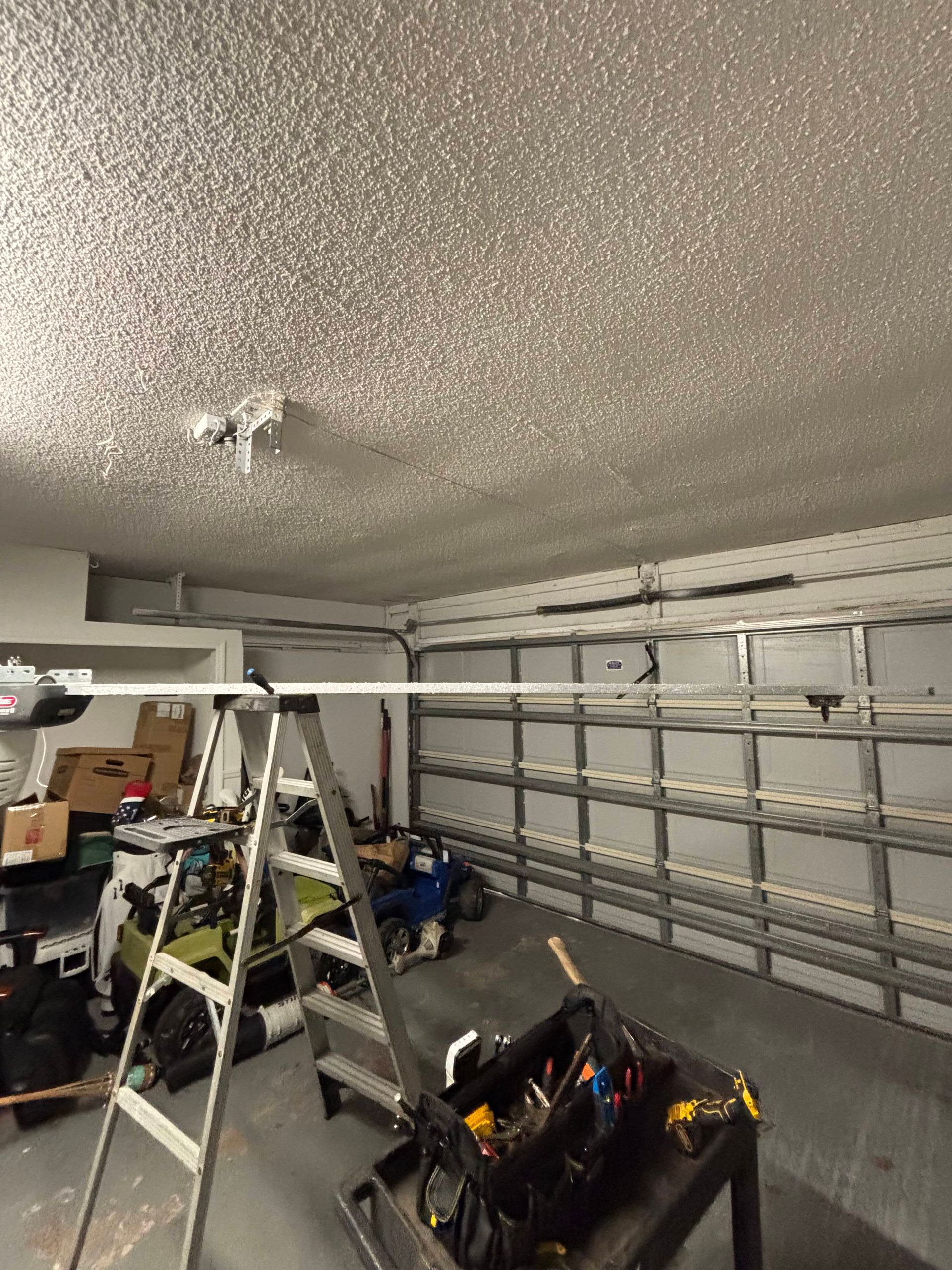 Garage interior with open garage door, ceiling light, ladder, and tools on a cart.
