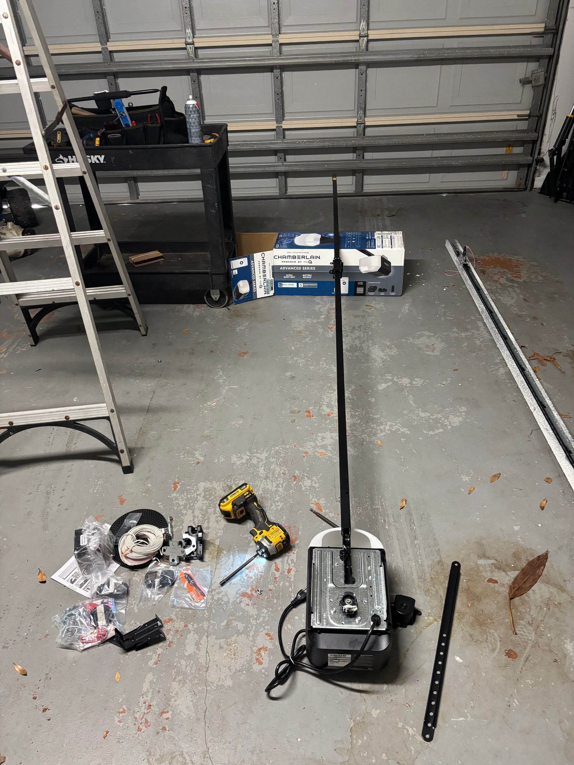 Garage workshop floor with scattered tools, a ladder, and long metal rails near a closed door