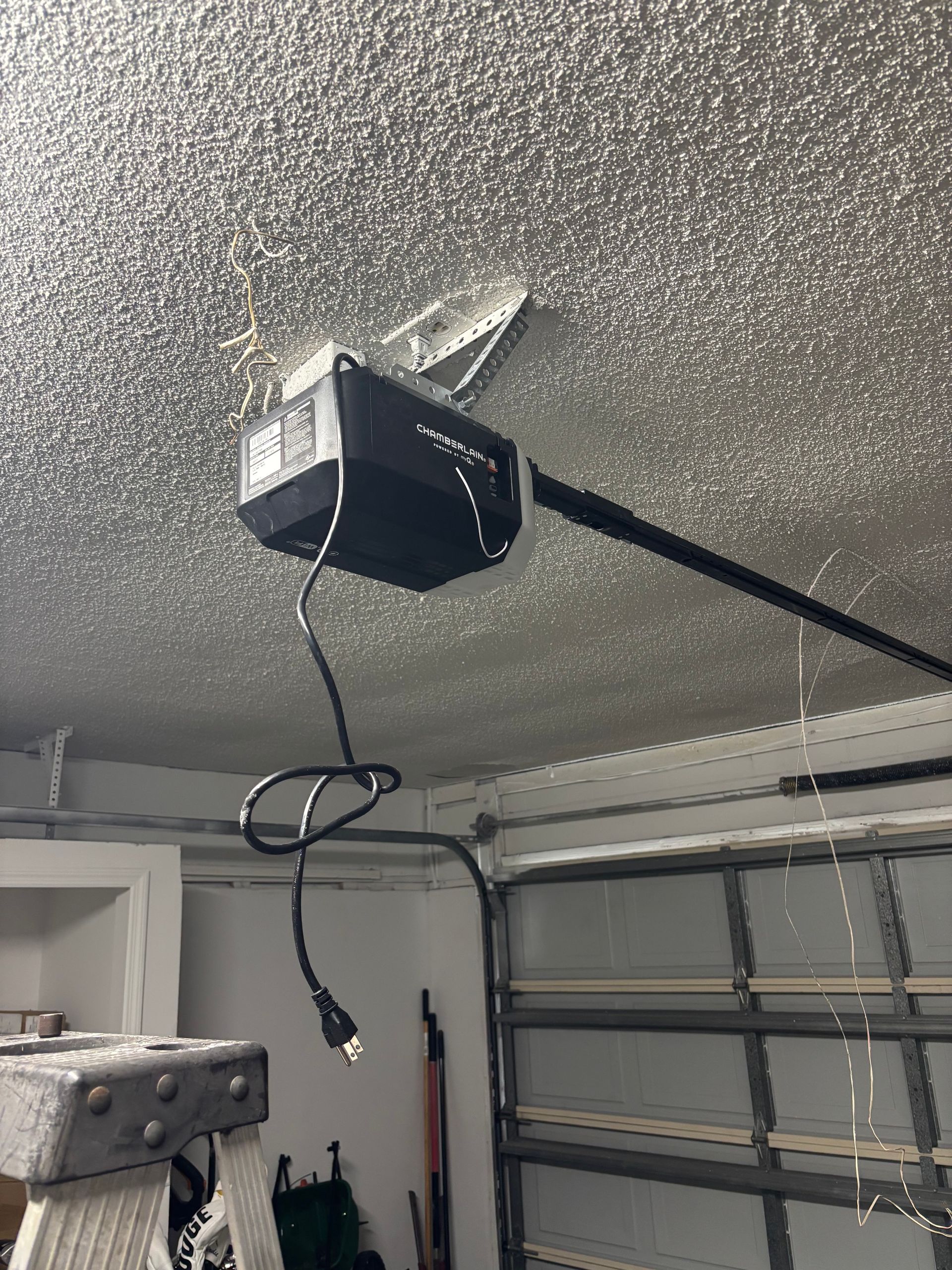 Garage door opener mounted on a speckled ceiling with a hanging cord.