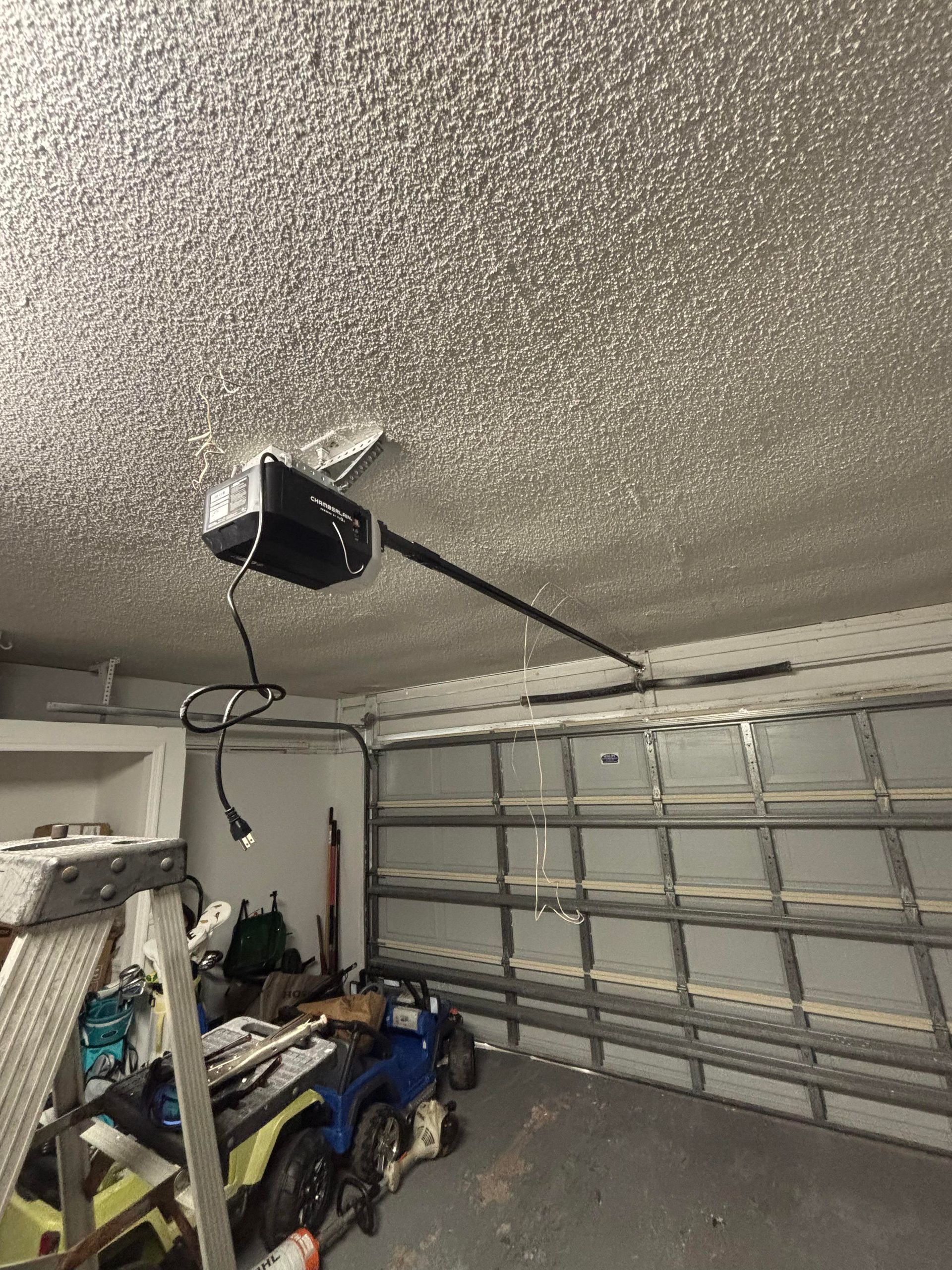 Garage interior with closed sectional door, textured ceiling, and overhead garage door opener.
