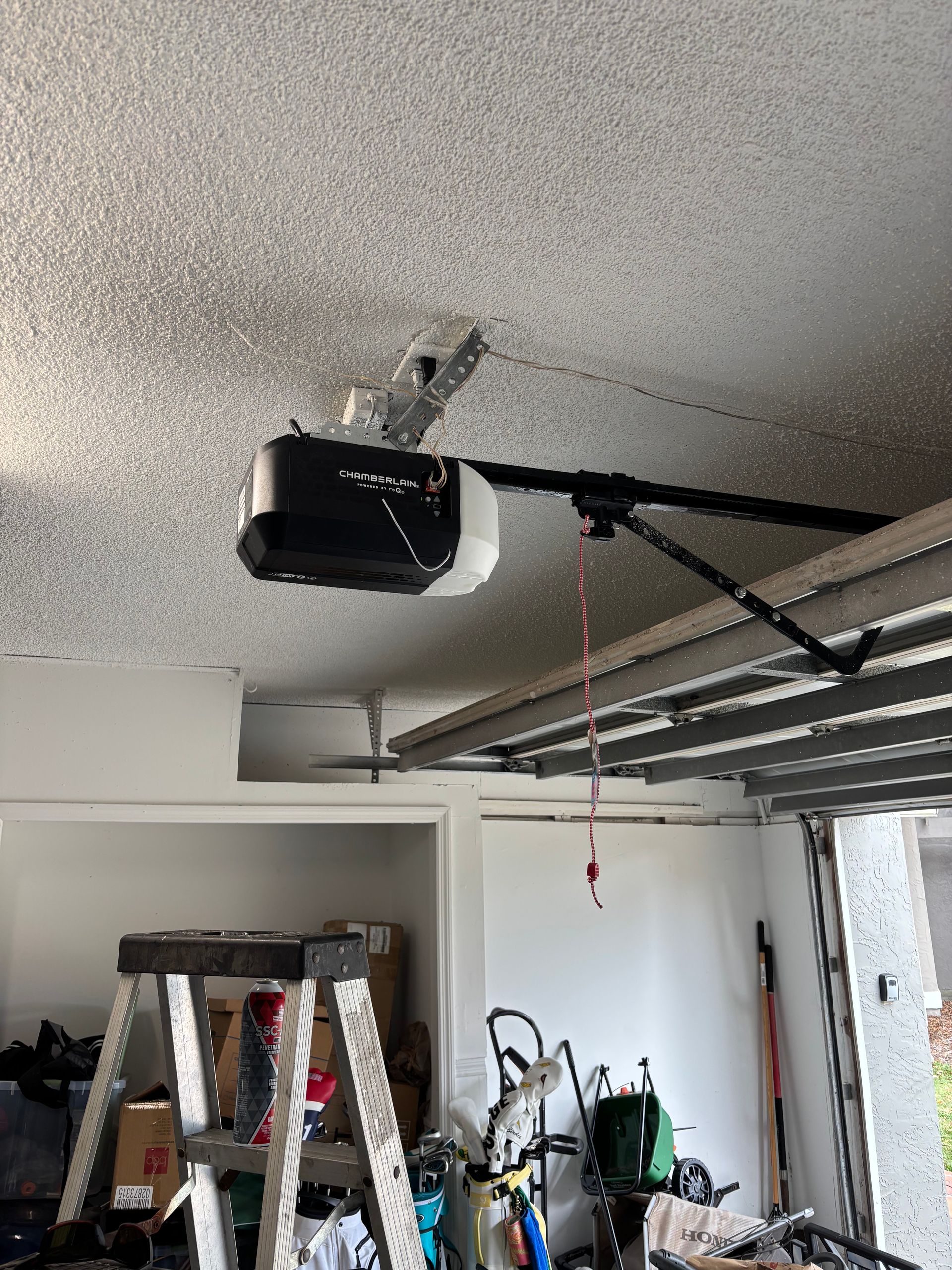 Garage ceiling with a black garage door opener and ladder below, near an open doorway.