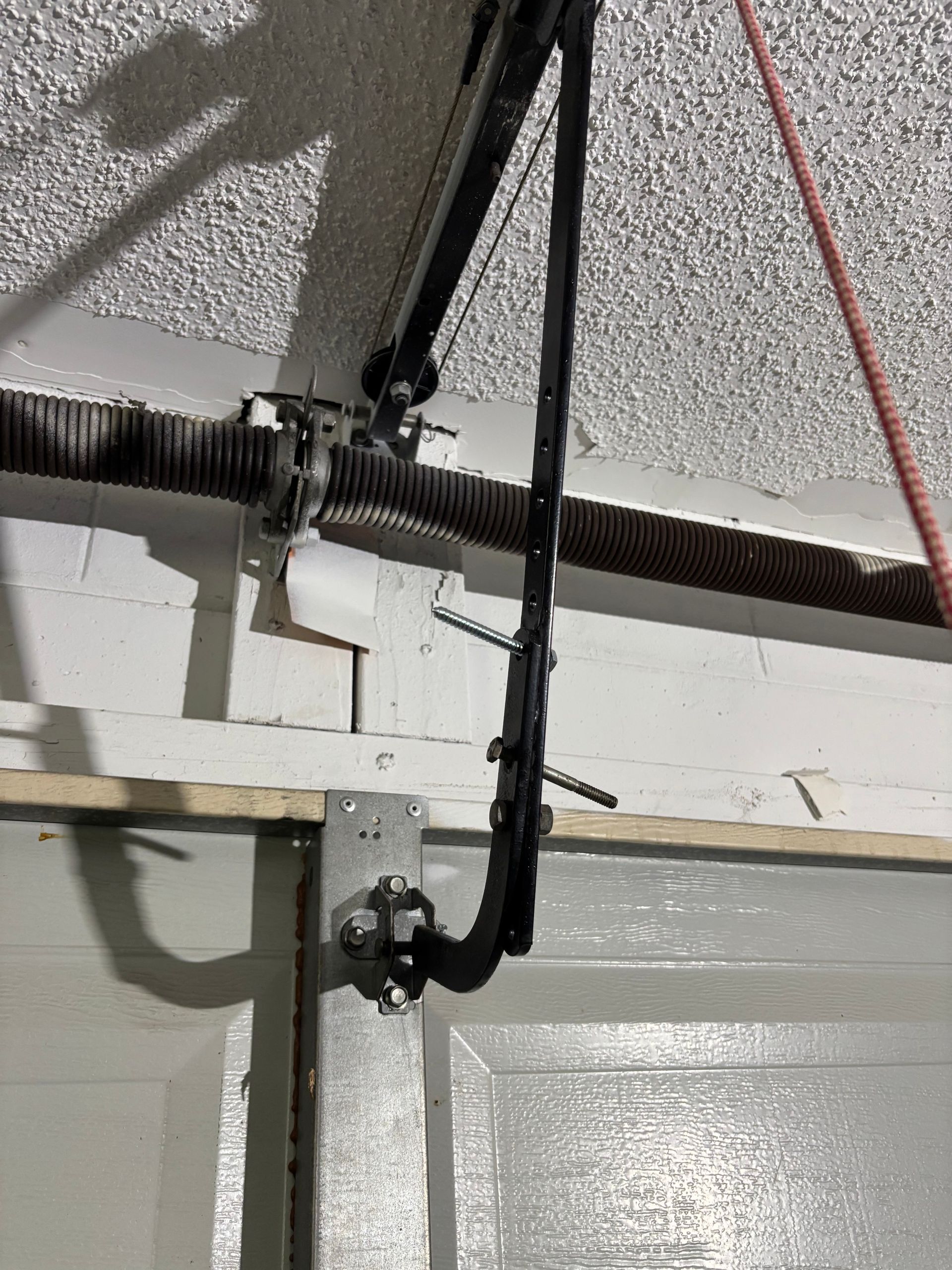 Close-up of a garage door torsion spring and cable assembly mounted above a white door.