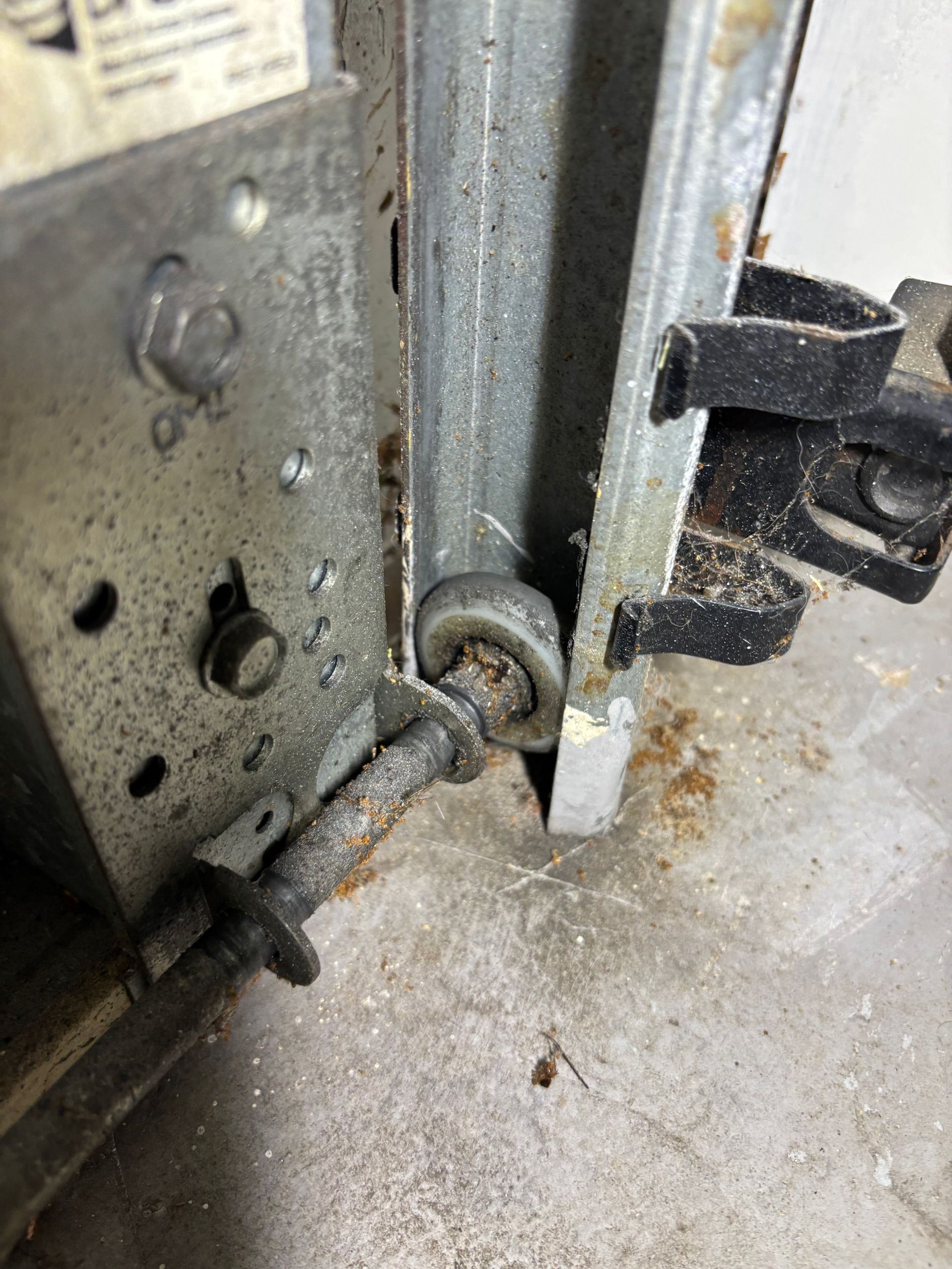 Close-up of a metal door hinge and latch on a worn, dirty floor edge.