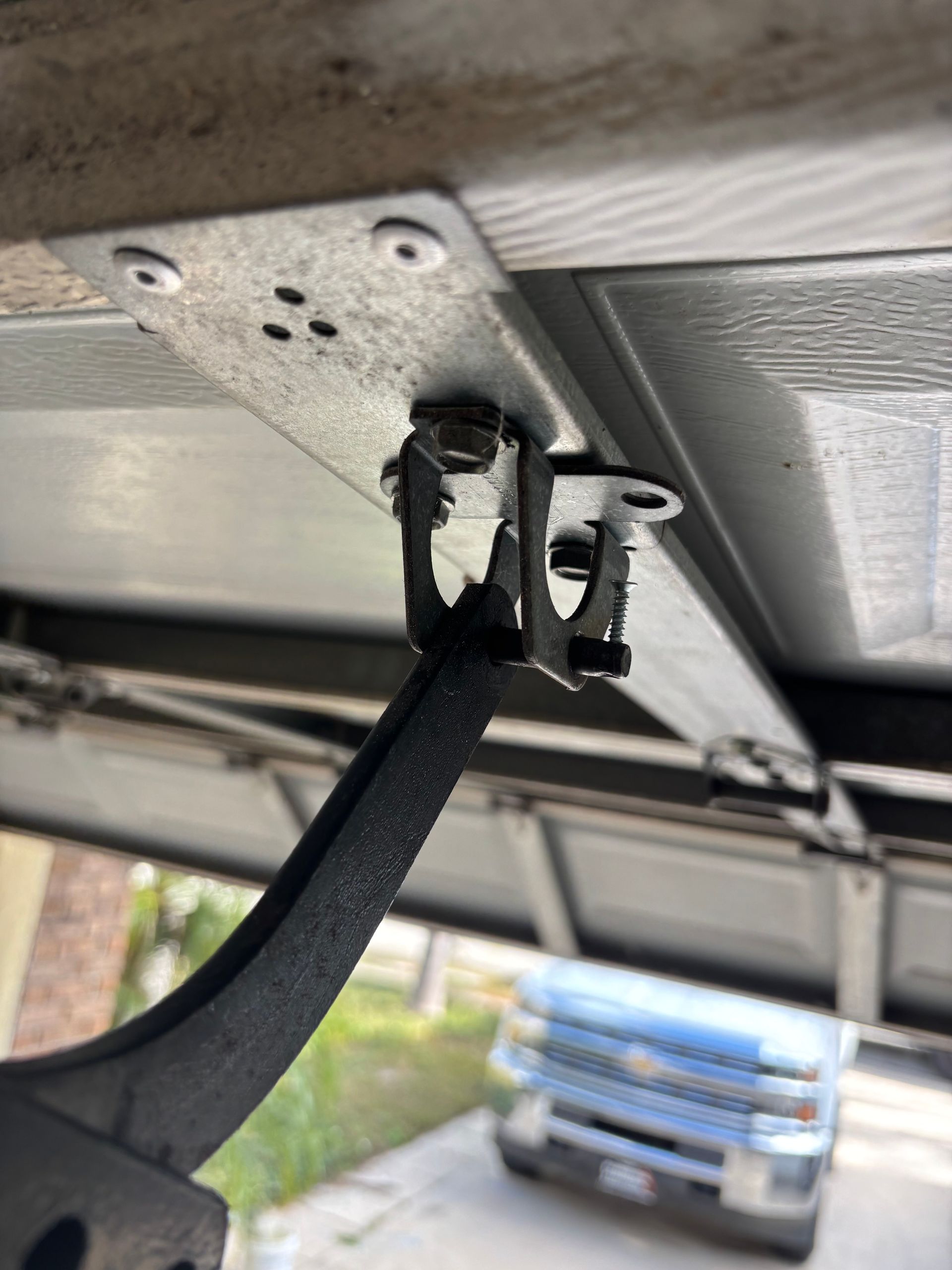 Close-up of a black metal bracket attached under a trailer or vehicle frame, with a pickup truck in the background