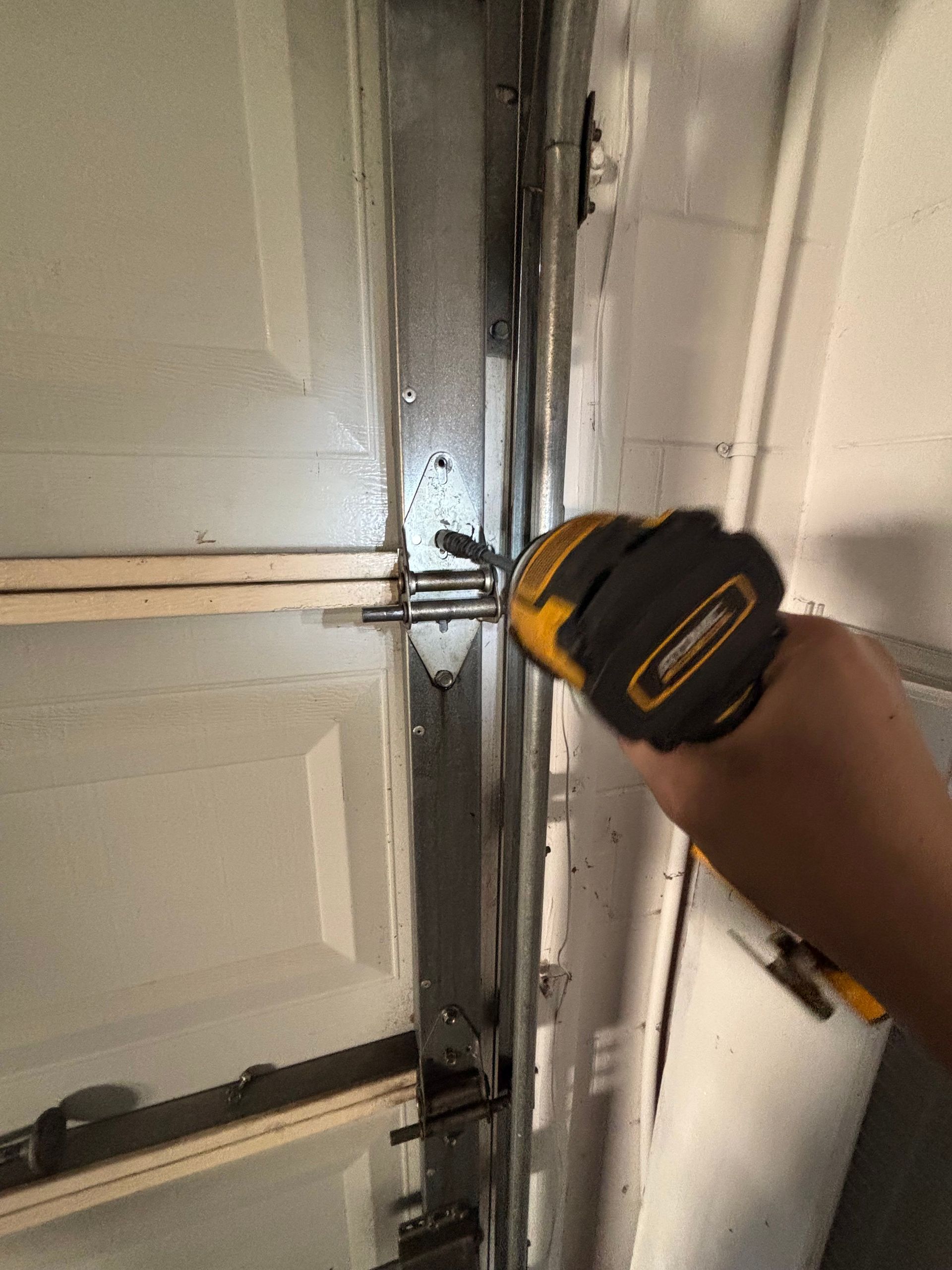 Hand using a drill on a garage door hinge or track during repair.