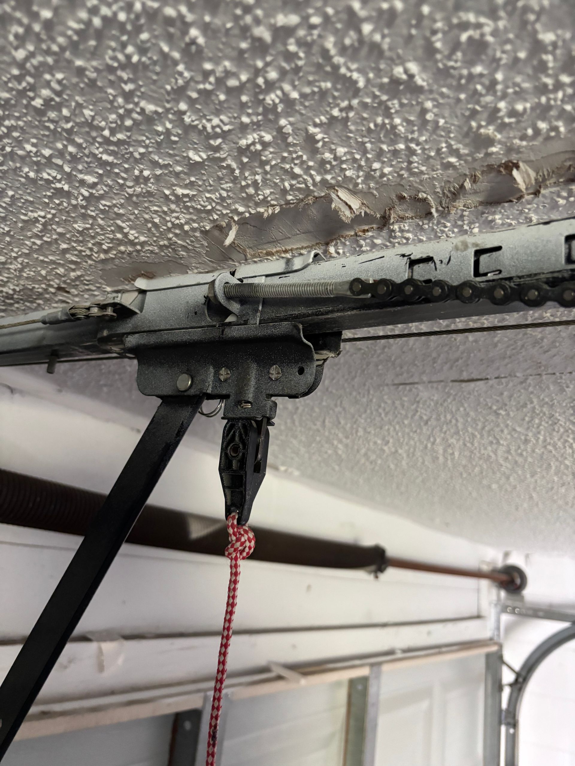 Close-up of a garage door opener bracket and cord mounted to a textured ceiling.