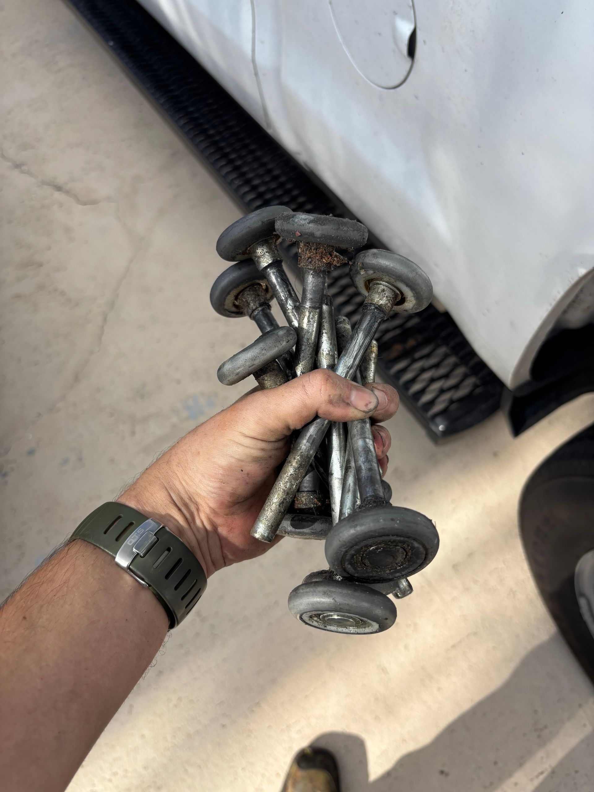 Hand holding several silver bolts beside a car door and running board