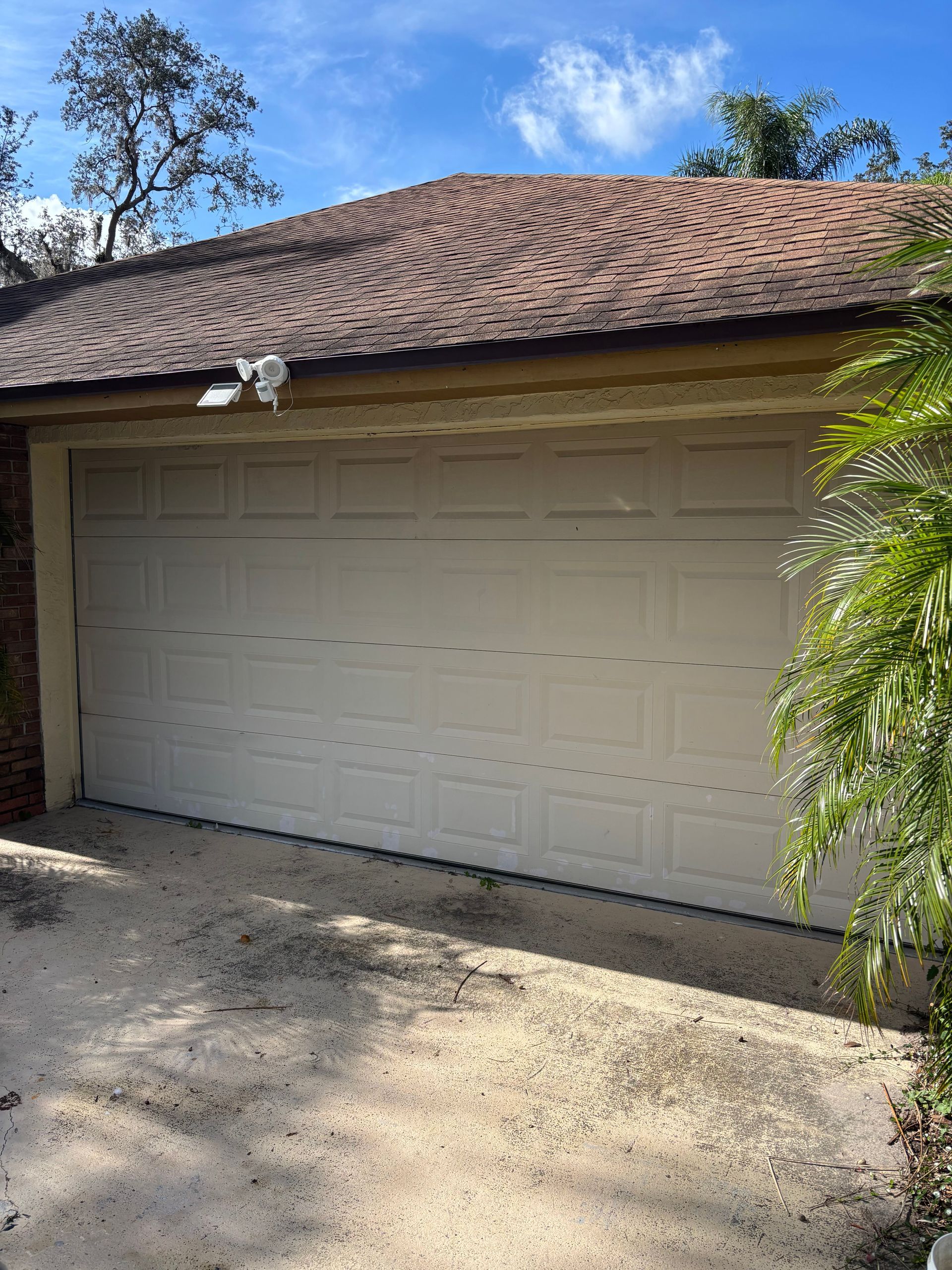 Closed white garage door on a tan house with a brown tiled roof and gravel driveway.