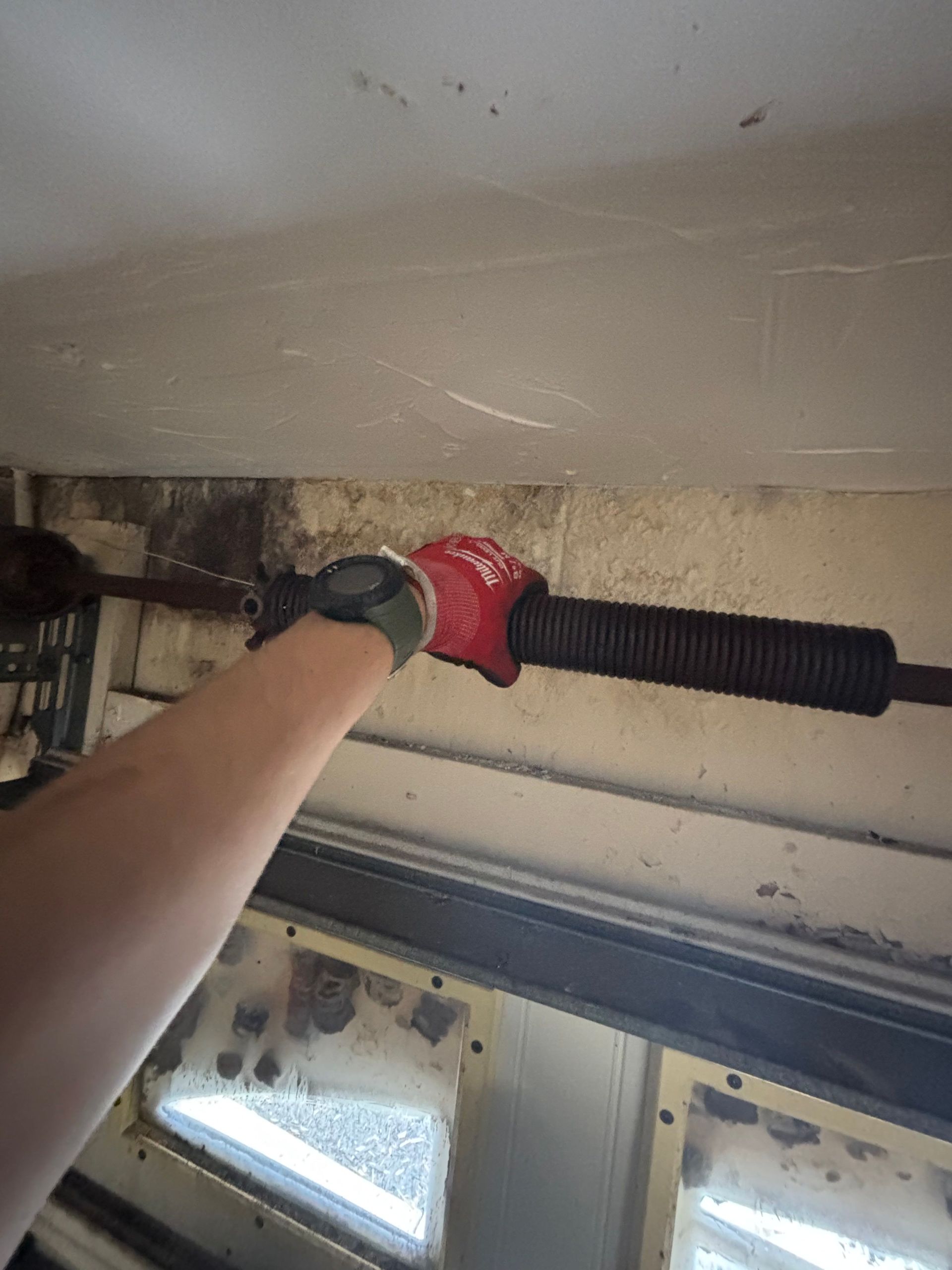 Arm in red glove holding a black window blind rod near a window frame