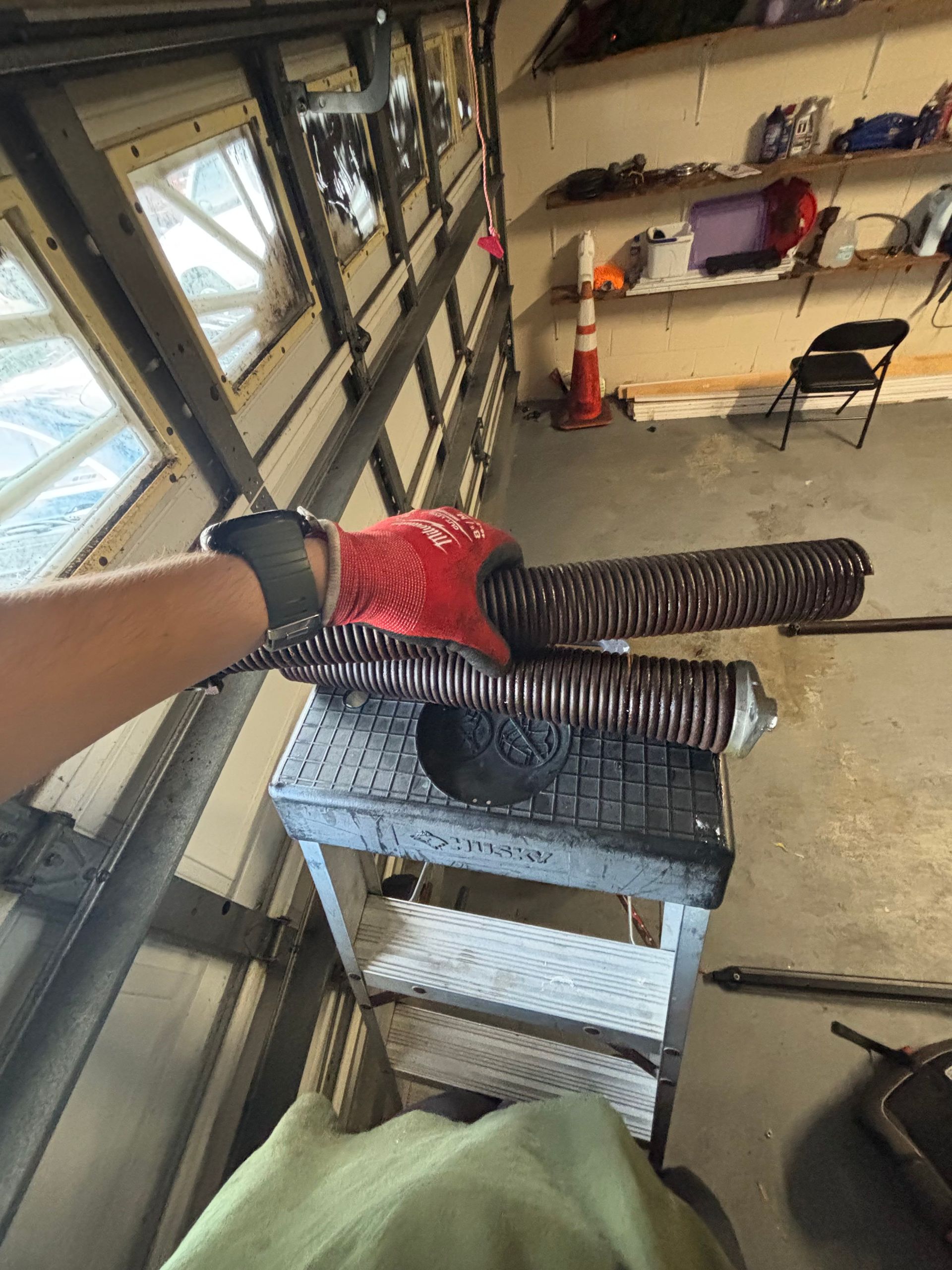 Gloved hand holding two black ribbed hoses over a cart in a garage or workshop