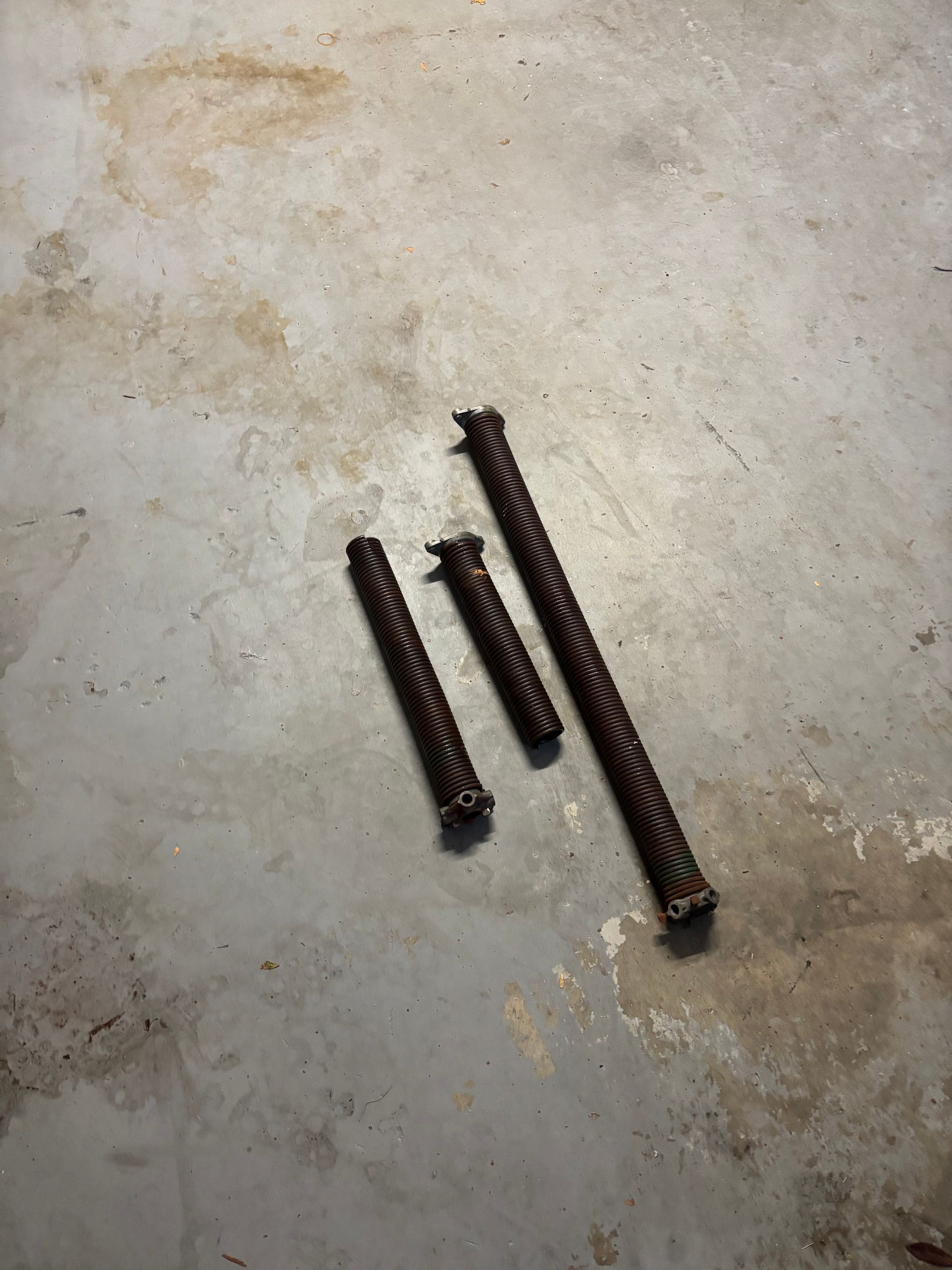 Three dark metal screws on a light concrete floor, arranged in a loose cluster.