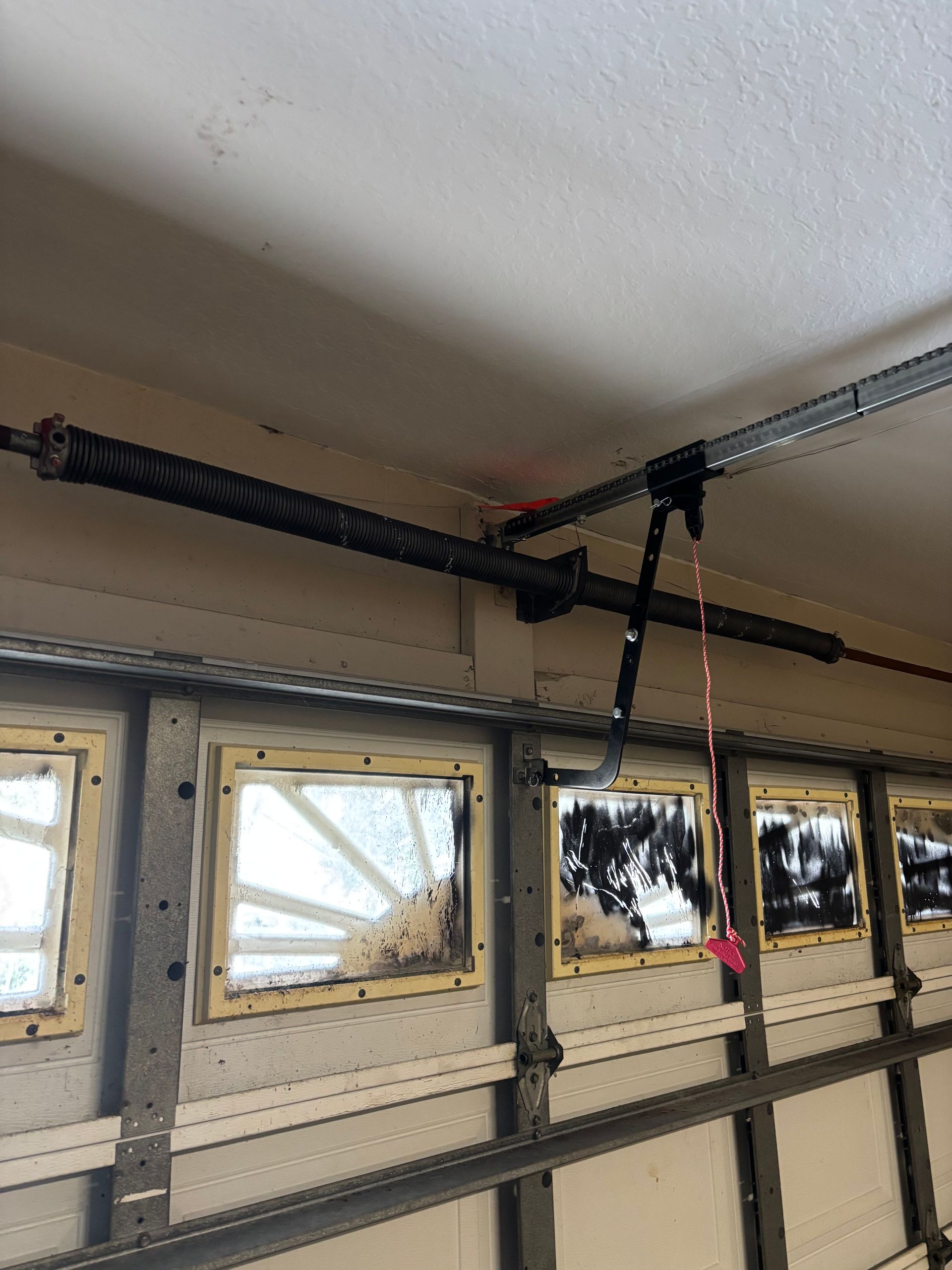 Garage ceiling with black overhead door springs and a hanging red pull cord above windows.