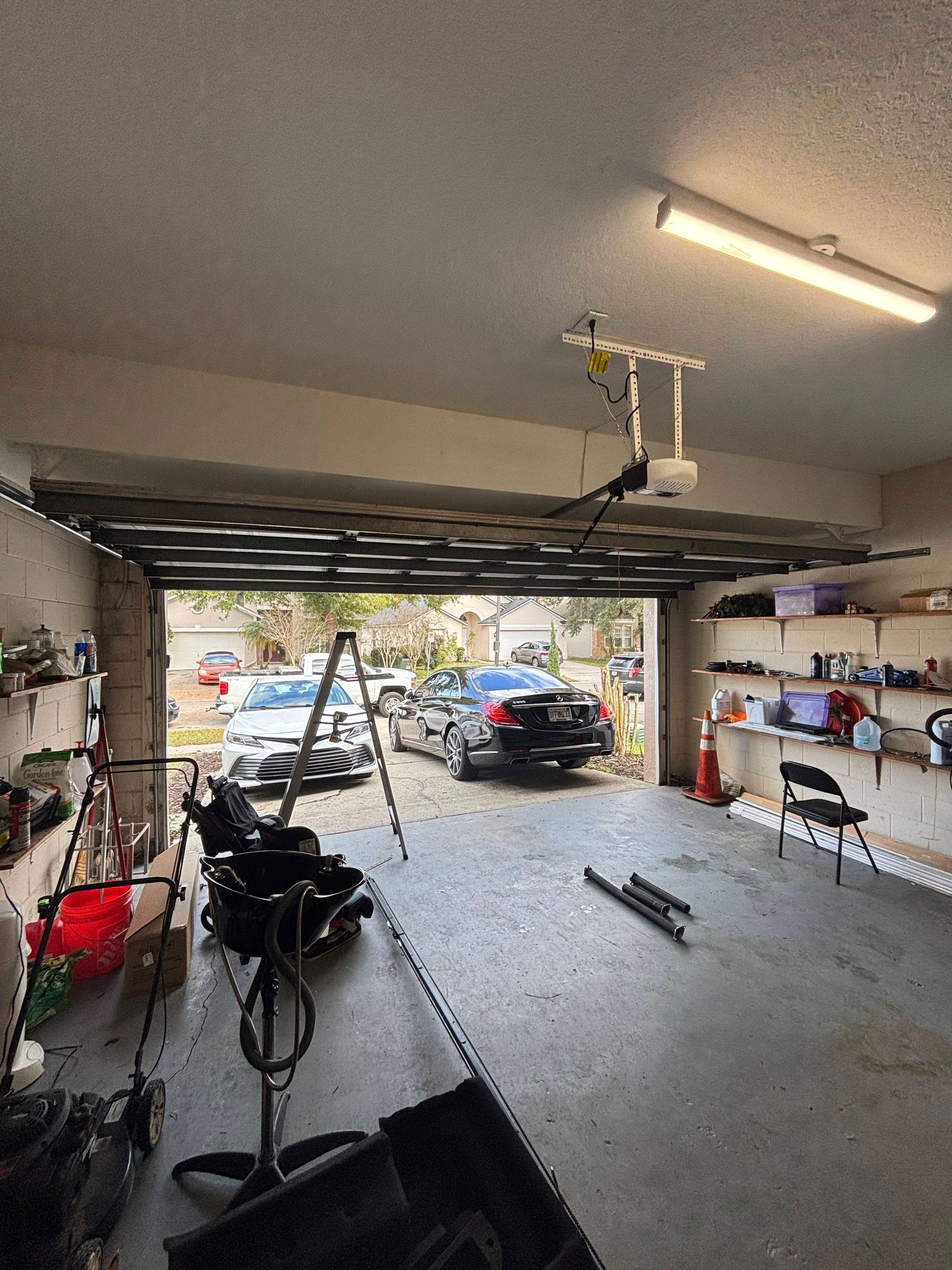 Garage interior with a car, bicycle, ladder, and tools, showing a partially open garage door.