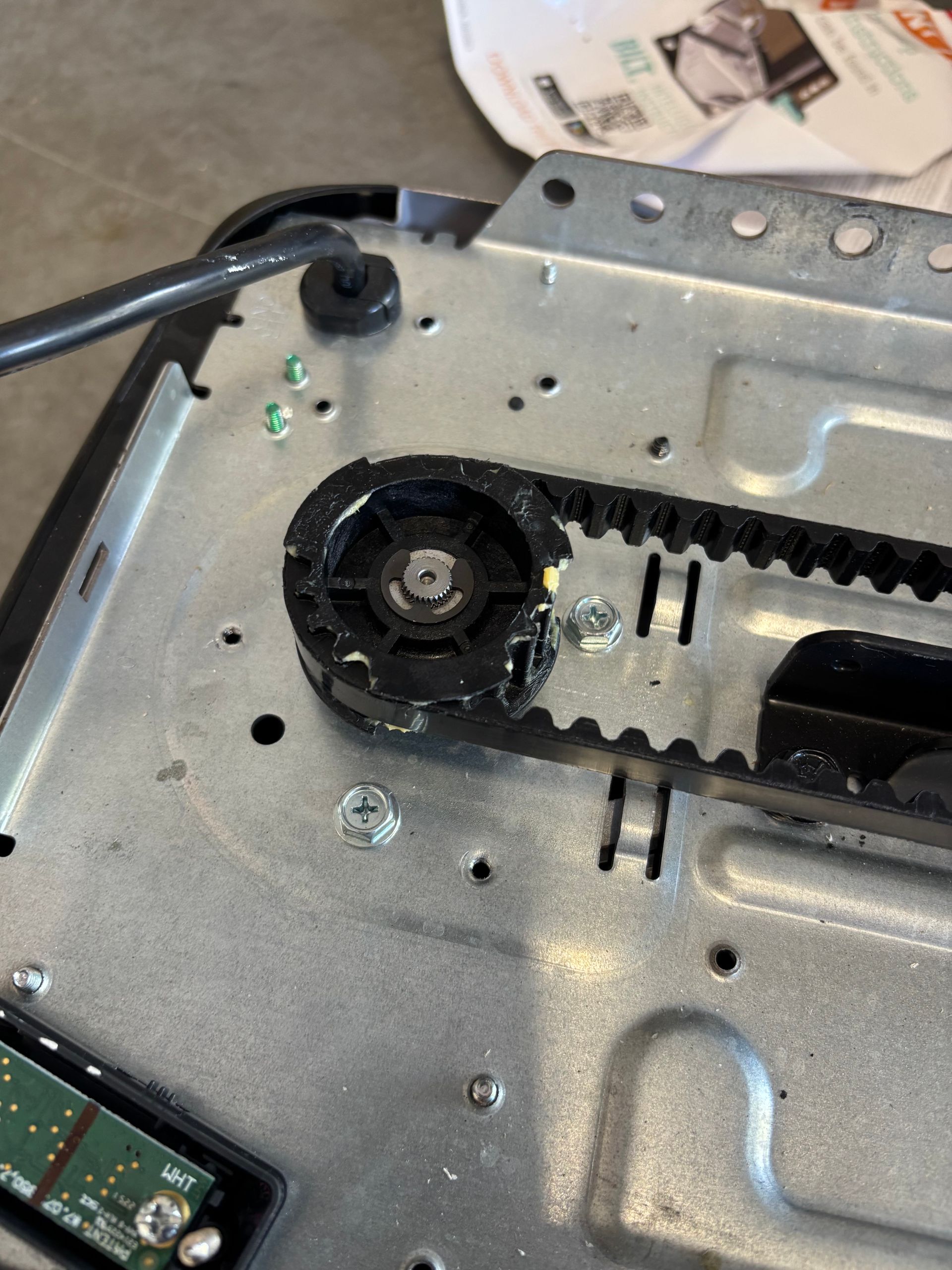 Close-up of a metal mechanism with a black gear, chain, and wiring inside an electronic device