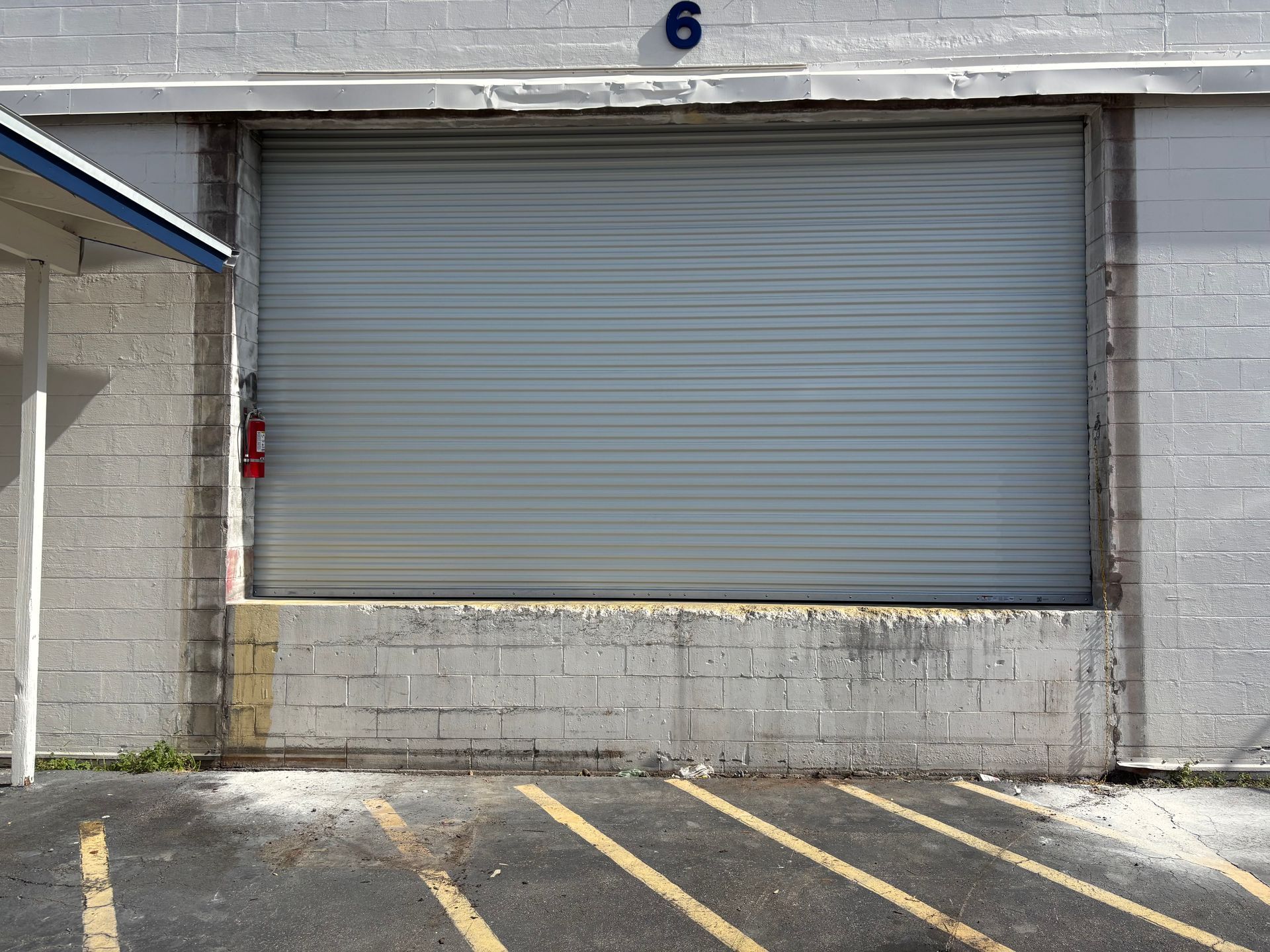Closed gray warehouse door with yellow-striped pavement in front, marked with the number 6 above it