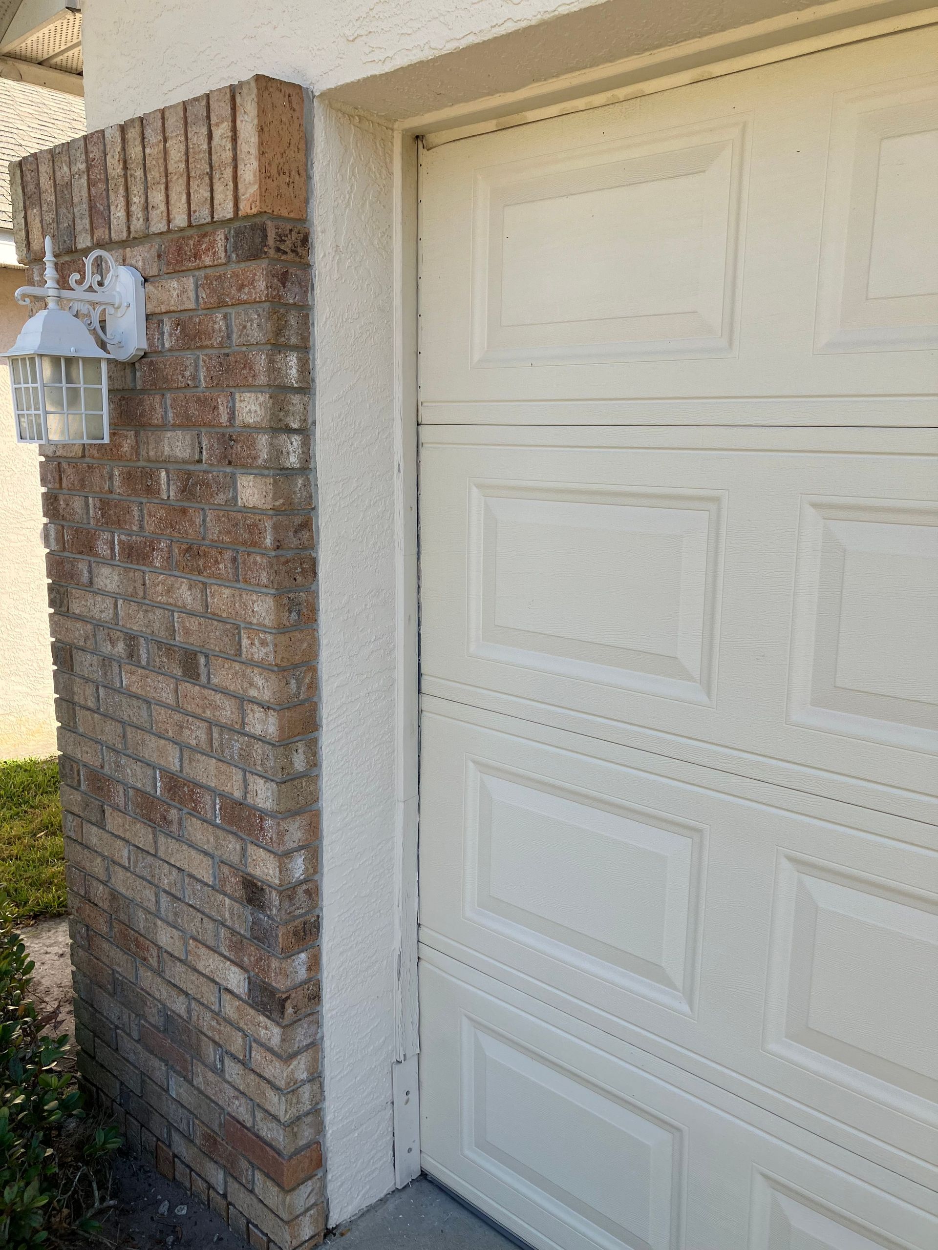 Brick house exterior with a white garage door and wall-mounted light fixture