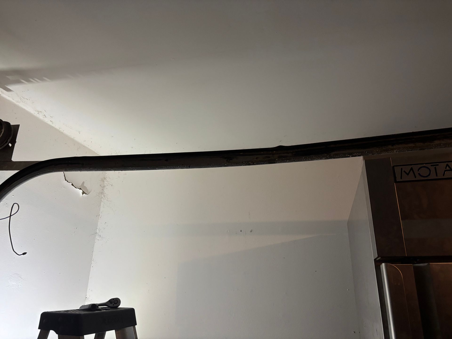White wall with a black cable running across the top and a dark wooden cabinet on the right