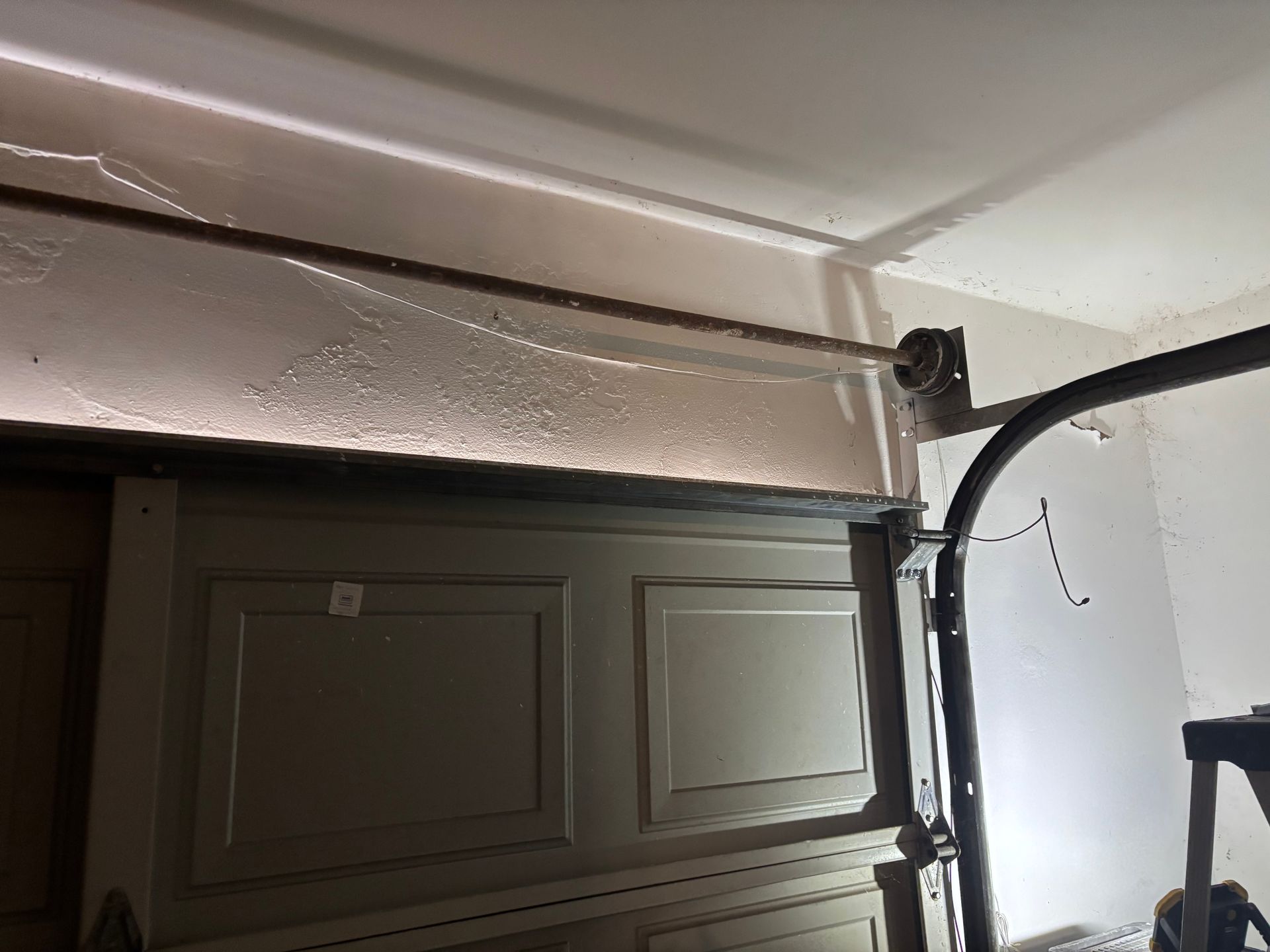 Garage door track and opener hardware near the ceiling, with a white textured wall and dark door panel.