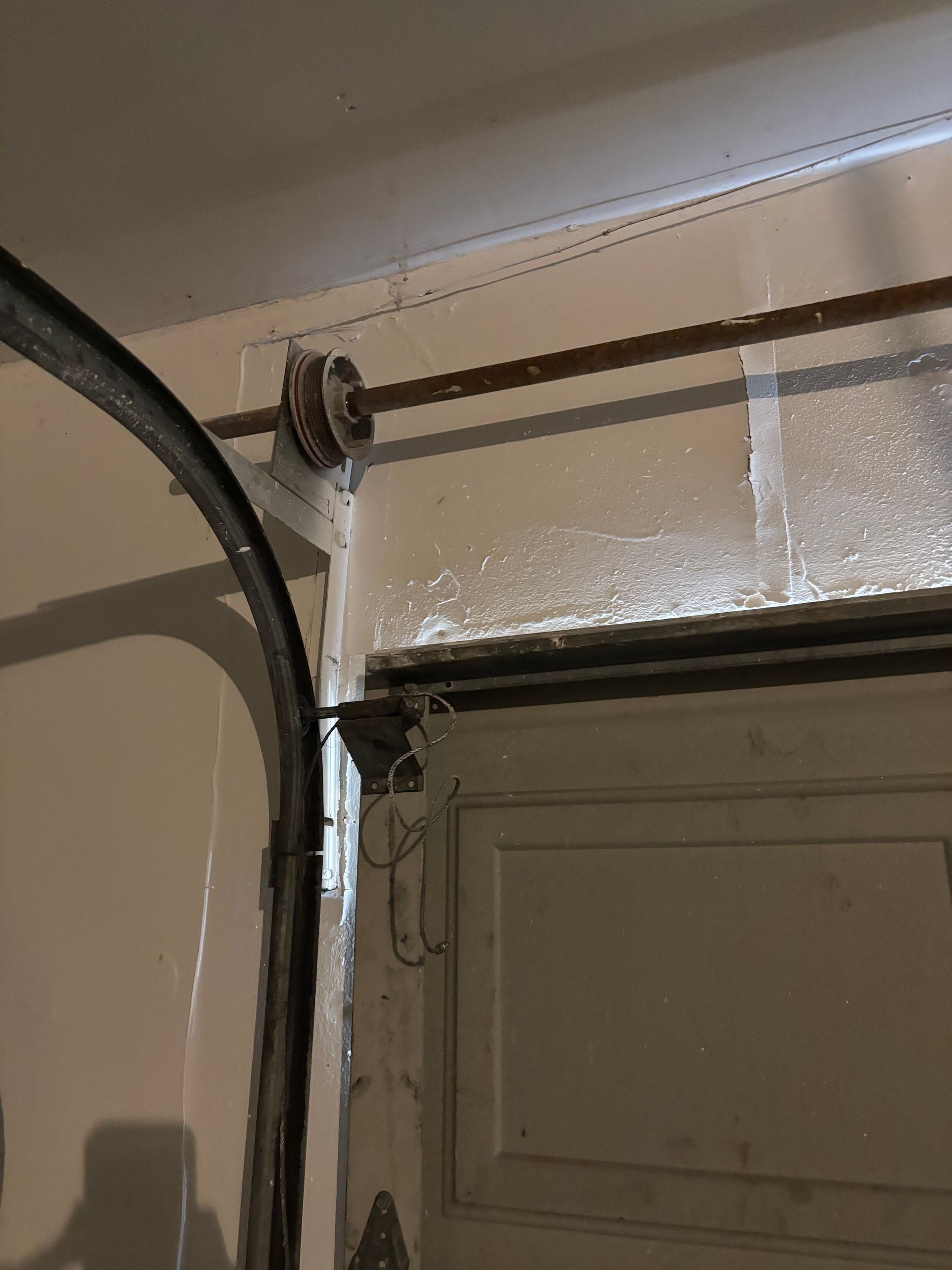 Garage door corner with metal track and hinge near a beige wall and doorway