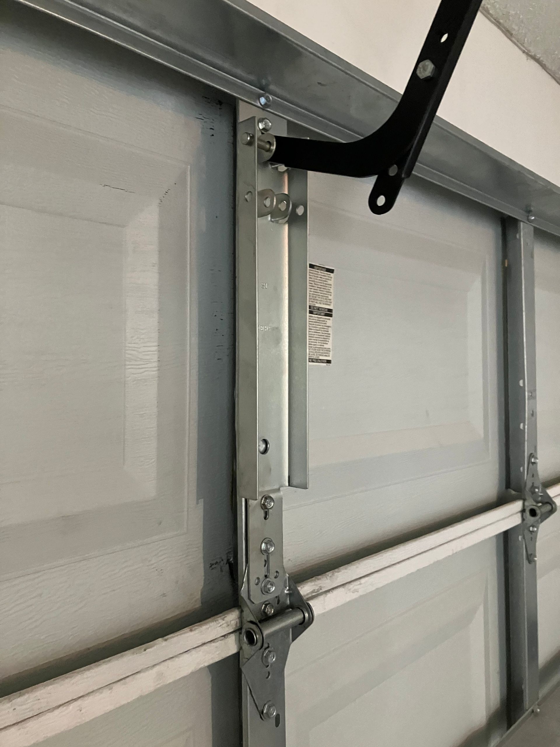 Garage door close-up with a silver metal support bracket and black hinge on a gray panel.