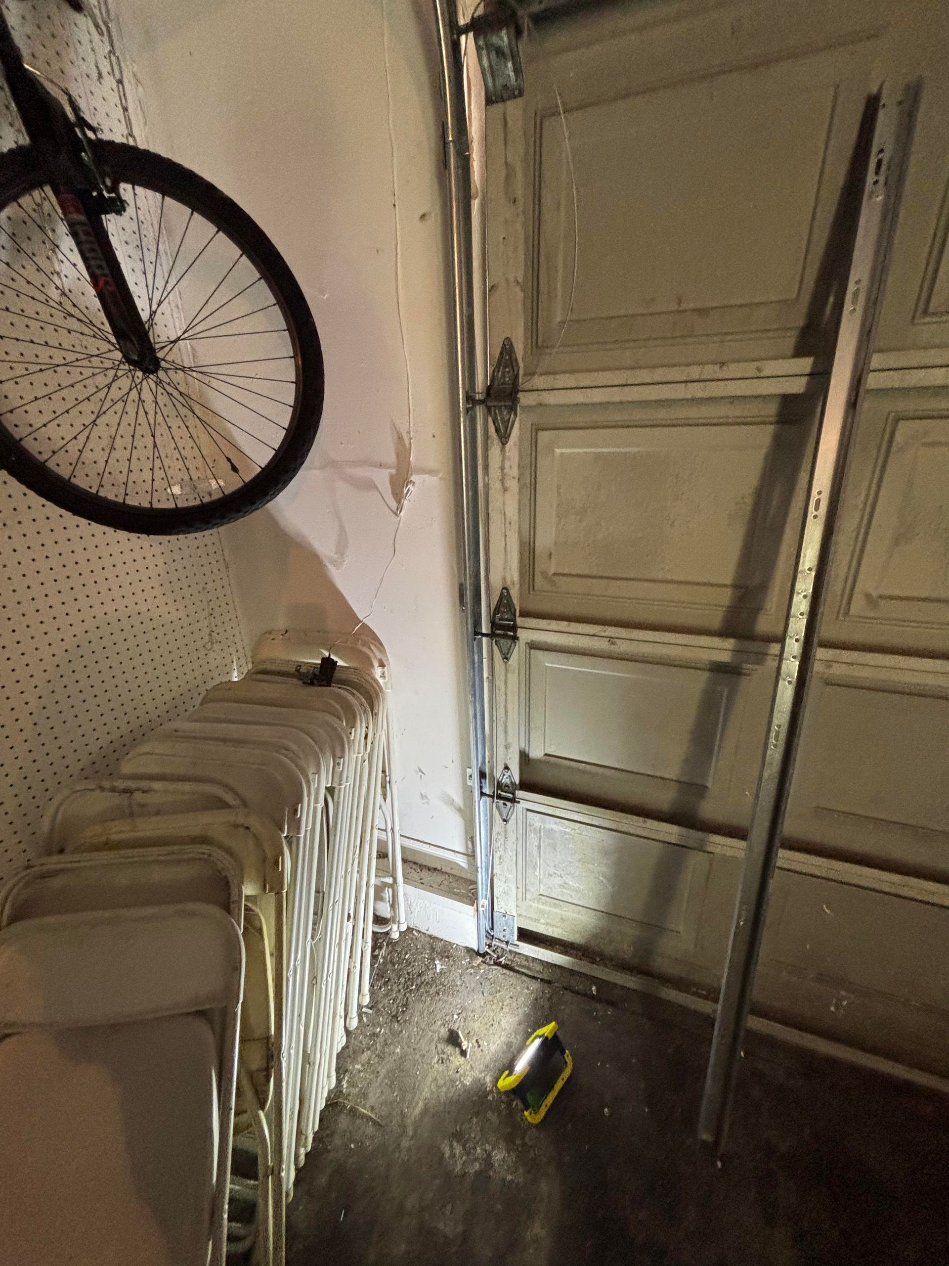 Tipped-over chairs beside a wall-mounted bicycle in a narrow garage or storage room.