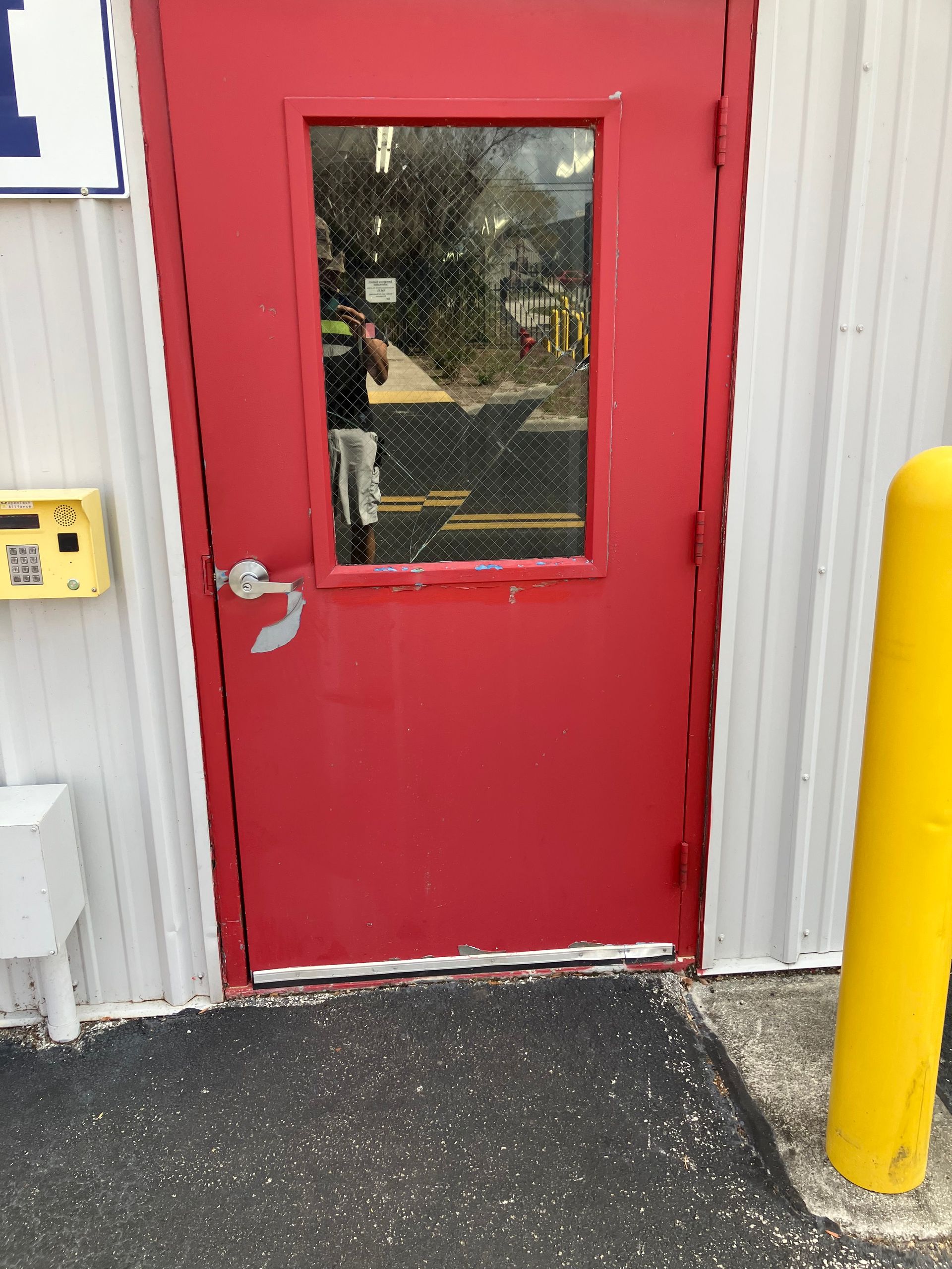 Red door with a window beside a yellow bollard at an industrial building entrance