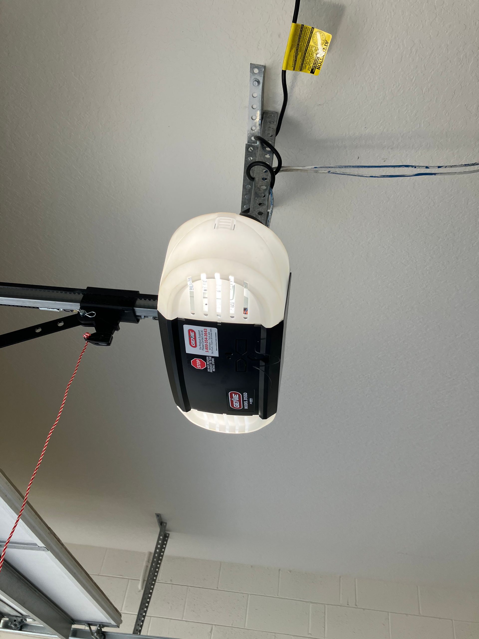 Garage door opener mounted on a ceiling with exposed cables and ceiling tracks