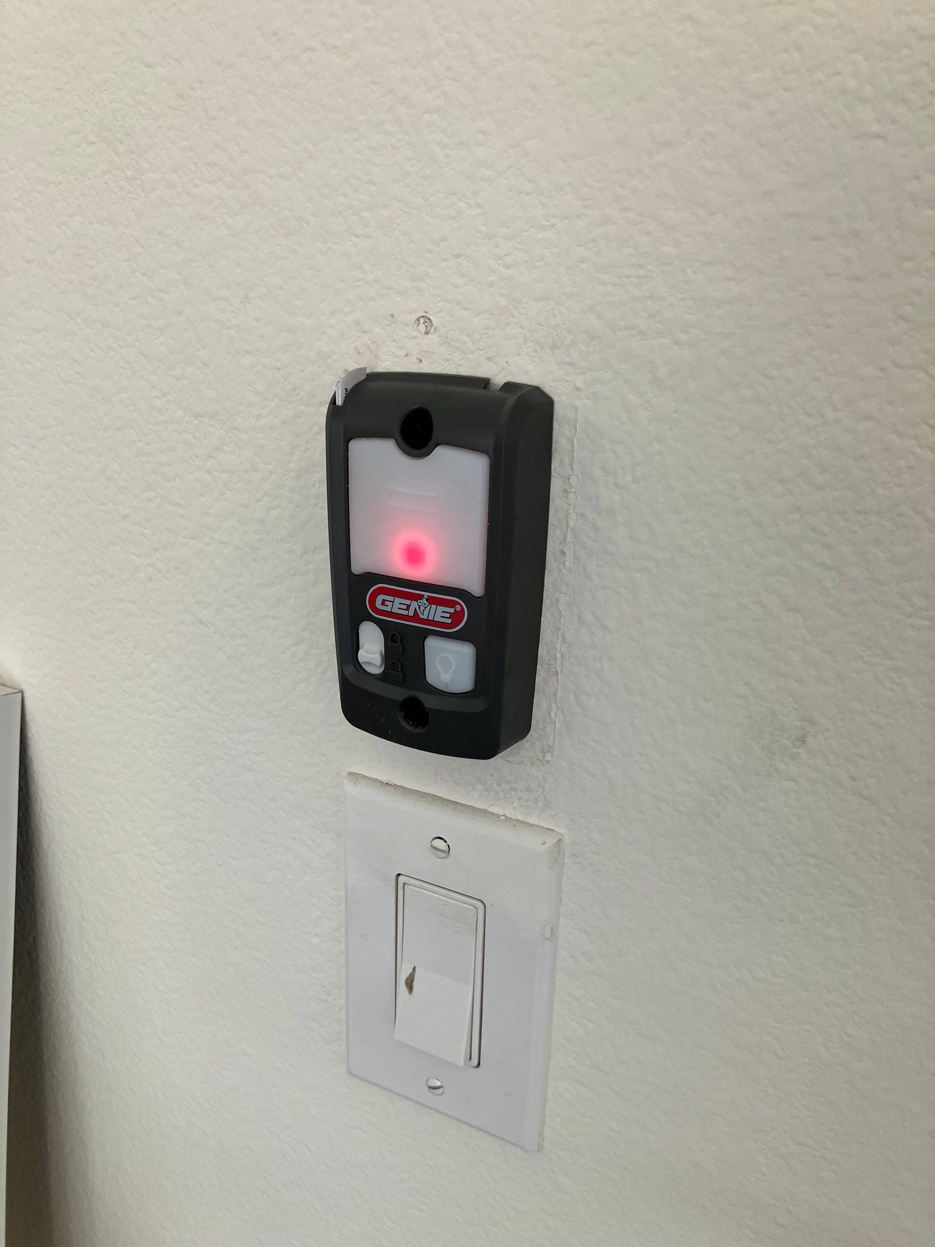 Wall-mounted access device with glowing red light above a white light switch on a beige wall