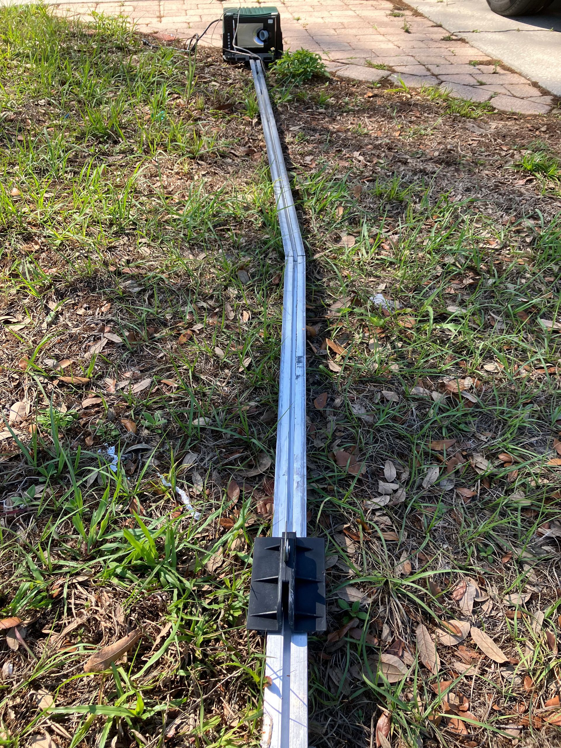 Long black pole or cable on grass, with a small device at one end and a clip in the middle.