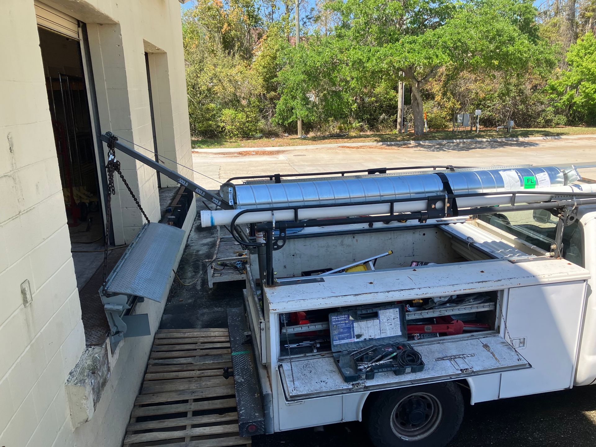 Utility truck with an extended boom parked beside a building and wooden pallets outside.