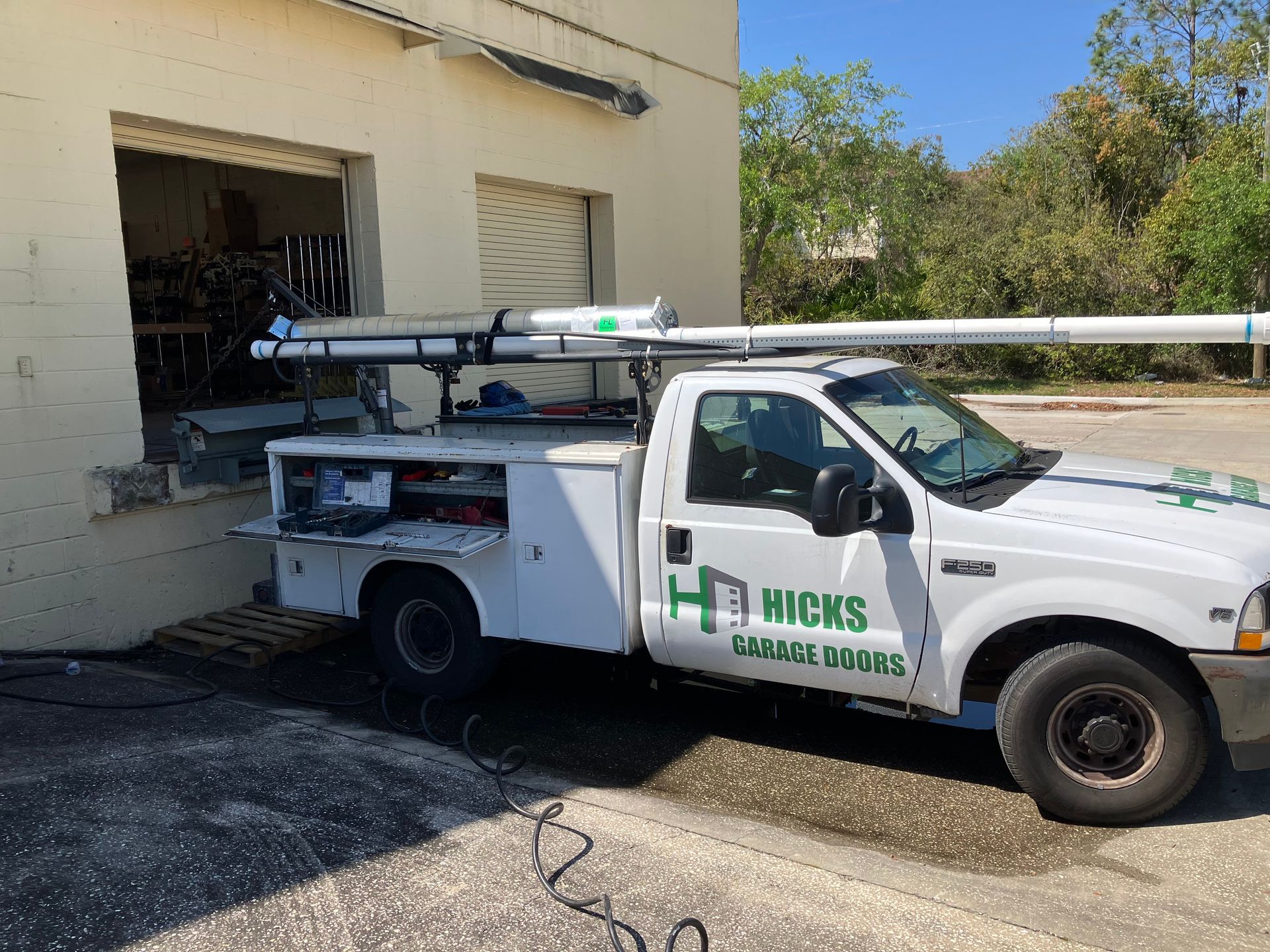 White utility truck with equipment parked beside a beige building with an open garage door