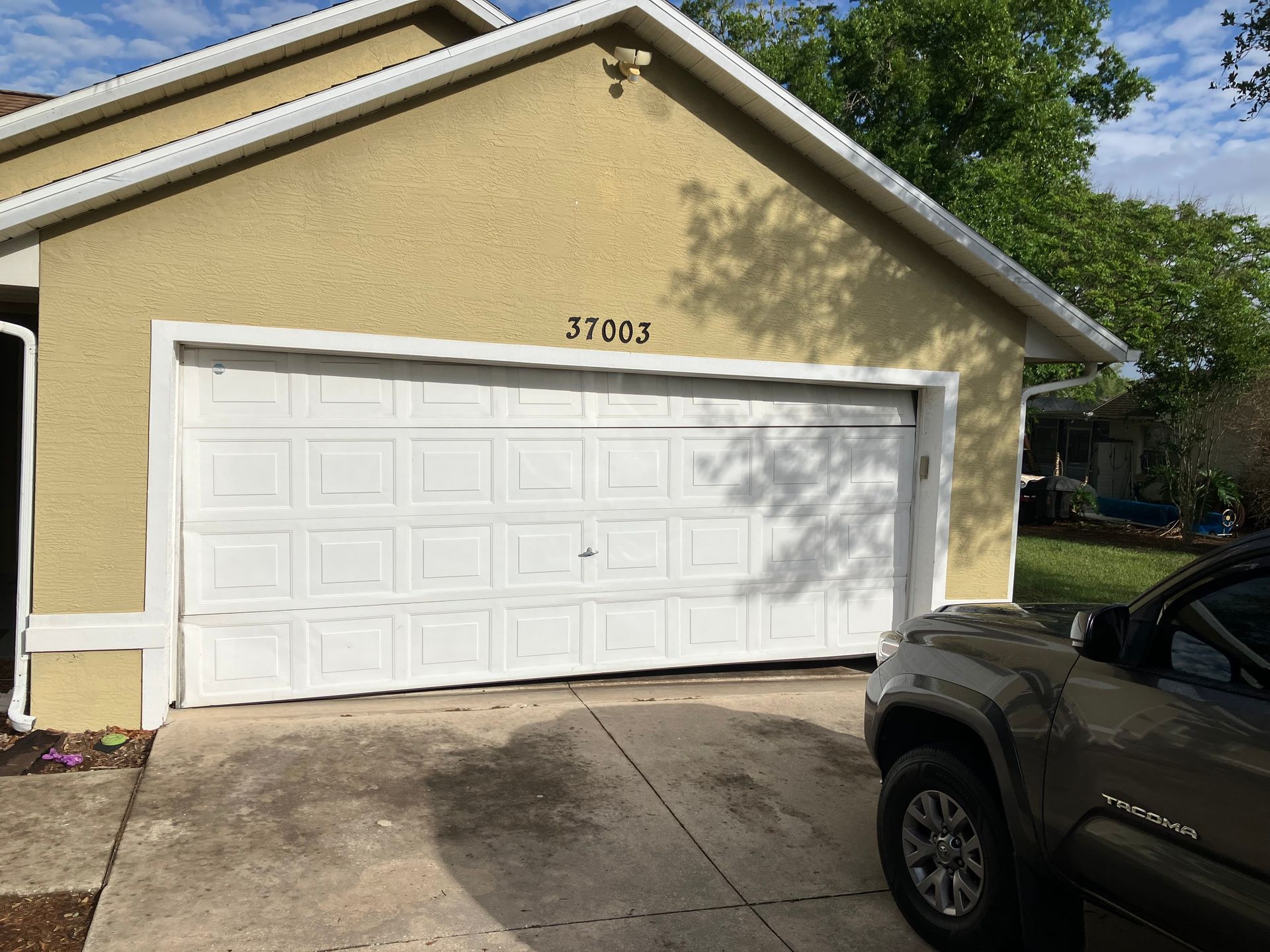 Yellow house with white garage door and a parked dark SUV in the driveway.