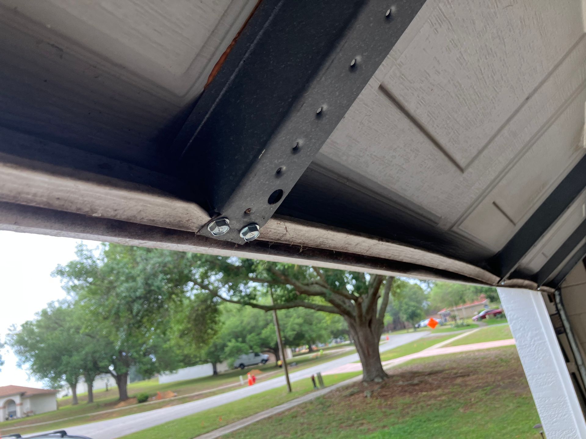 View from under a garage door into a suburban street with trees and orange traffic cones