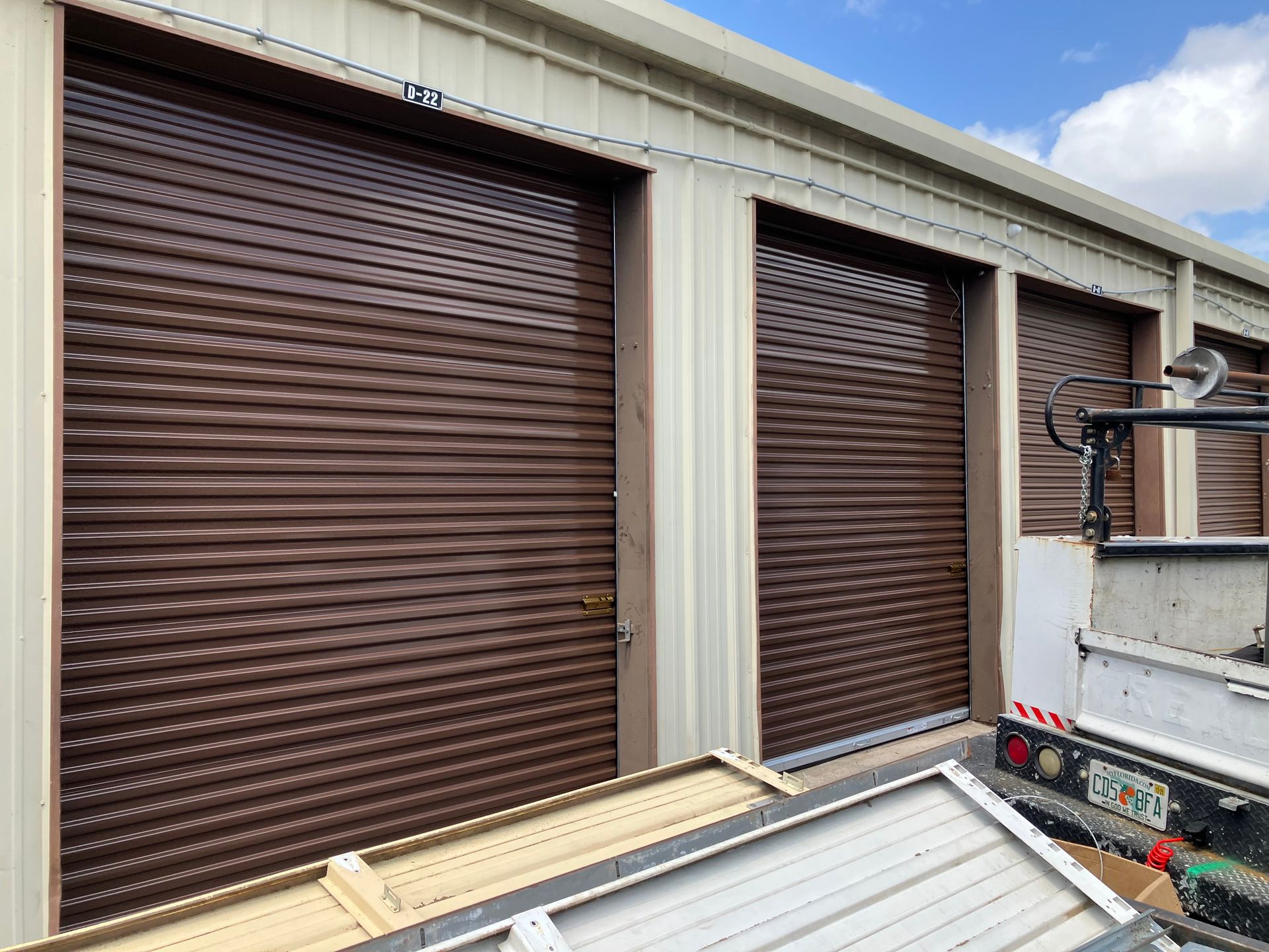 Brown roll-up storage unit doors beside a truck and building exterior under a blue sky