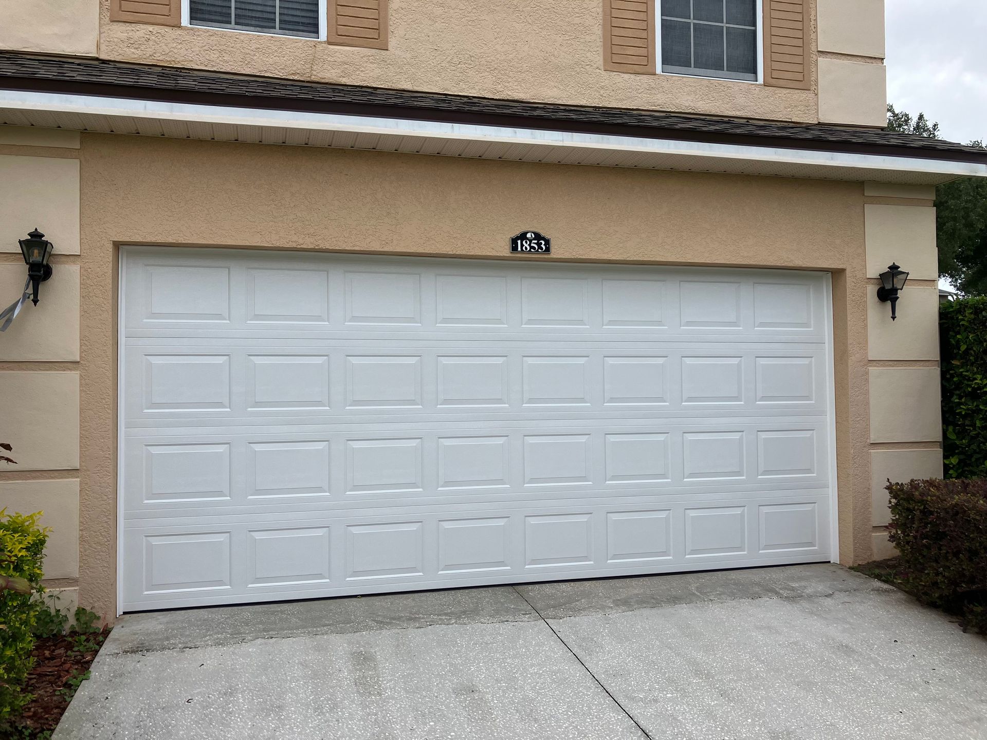 White double garage door on a beige house exterior with small wall lights and a sloped driveway