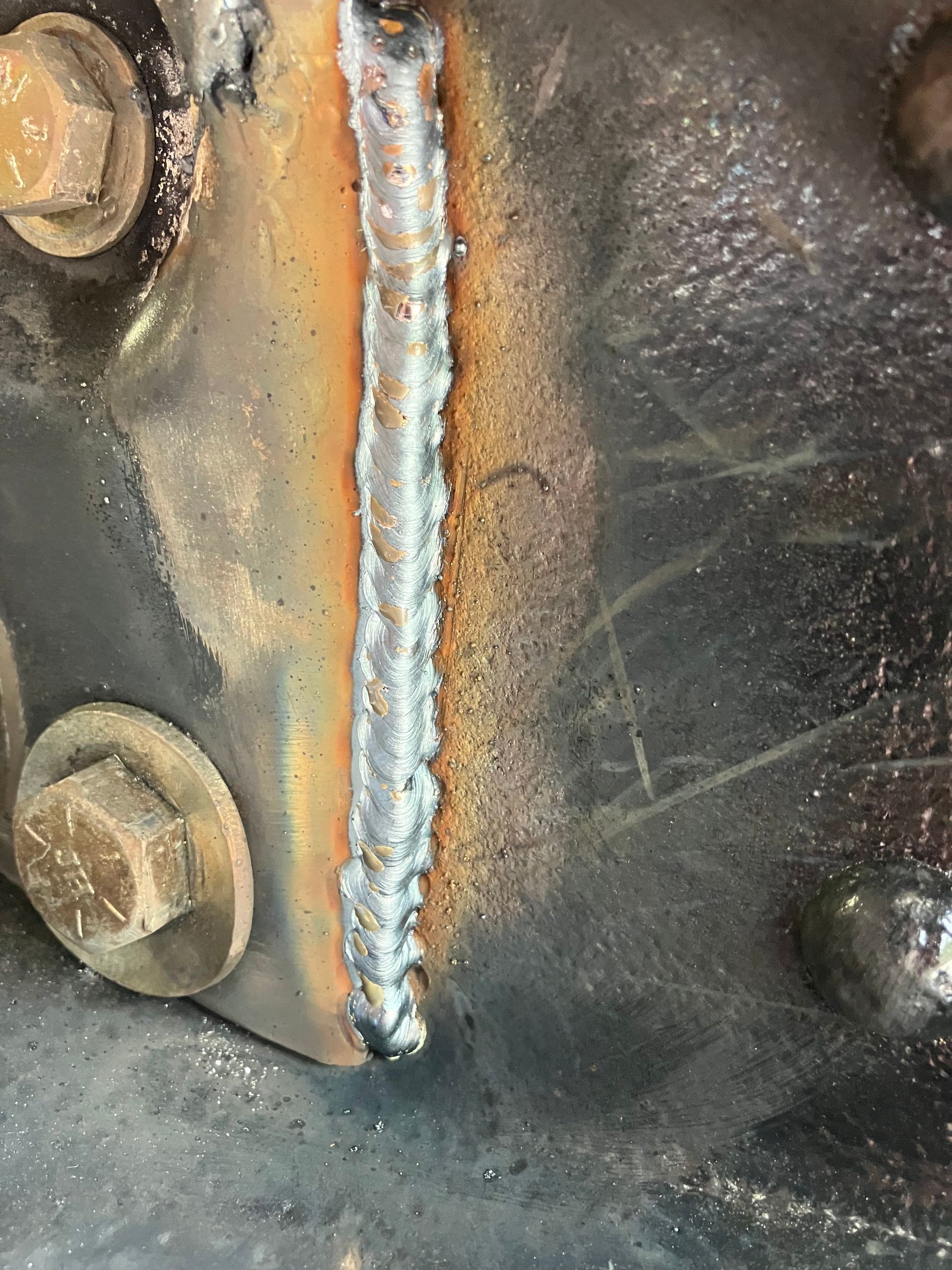 Close-up of a rusty welded seam on a black metal surface with two bolts.