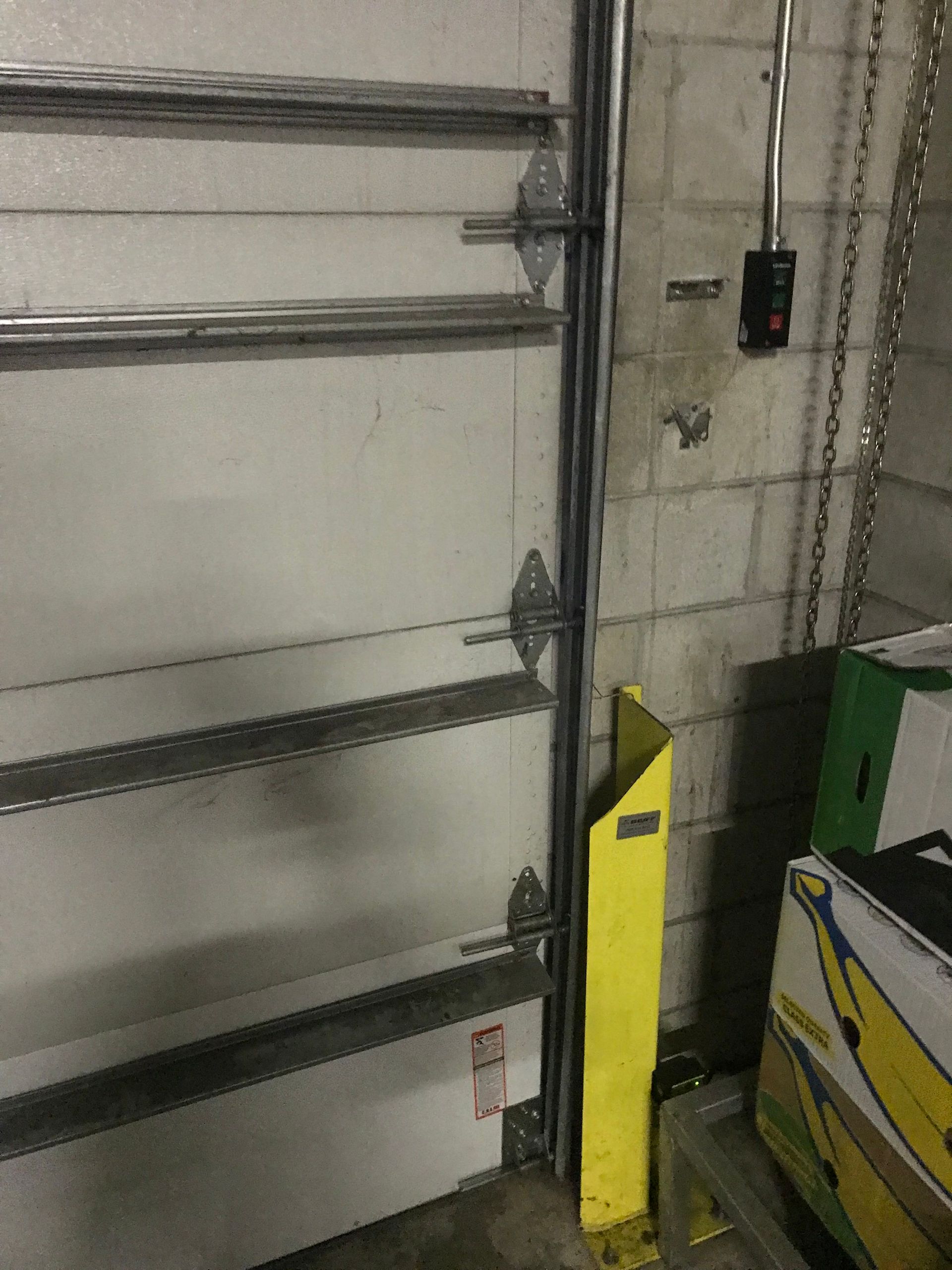 Industrial garage interior with metal shelving, a yellow safety bollard, and a green machine on the right.