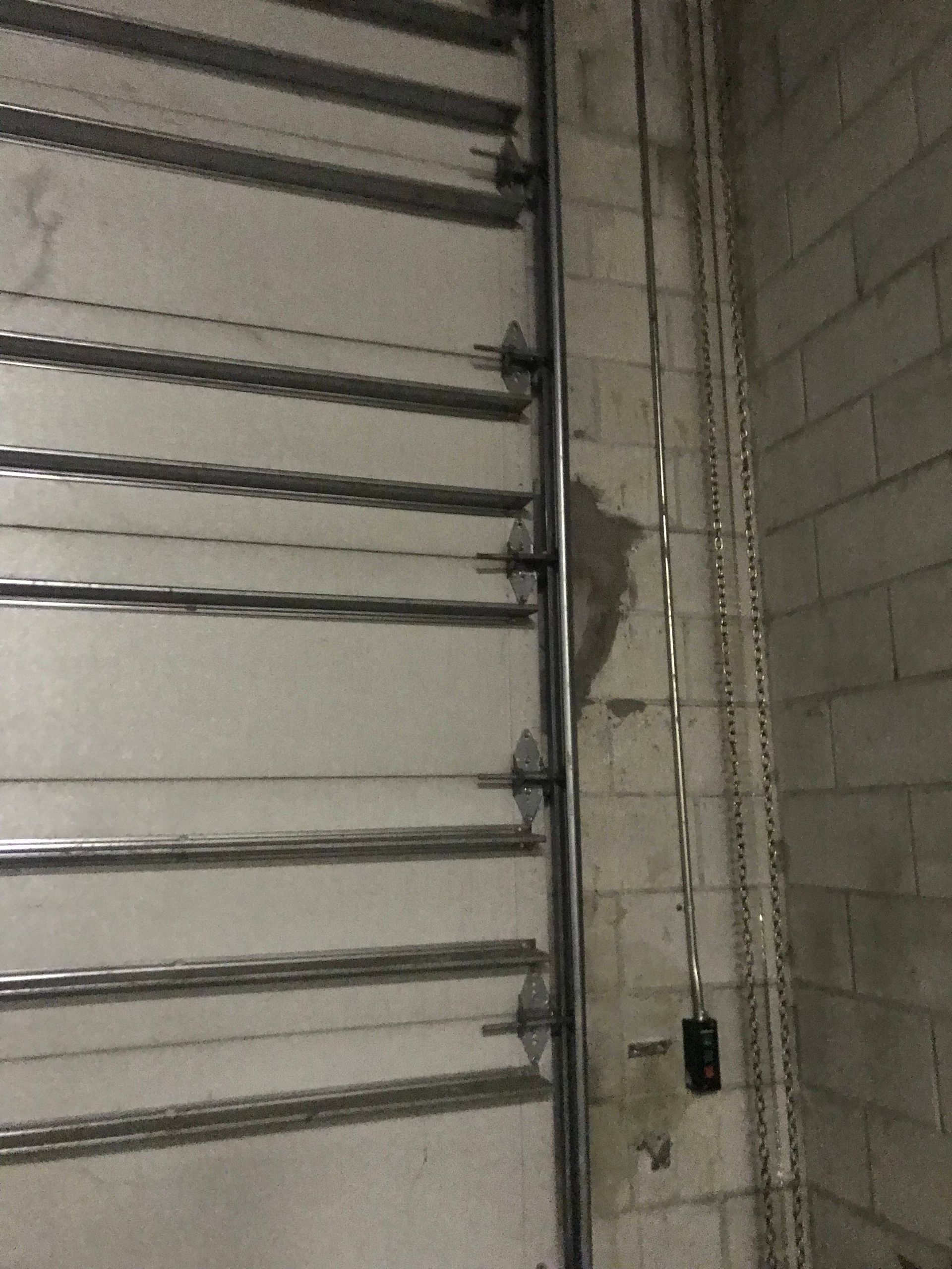 Garage wall with a metal roll-up door and exposed wiring by a concrete block wall