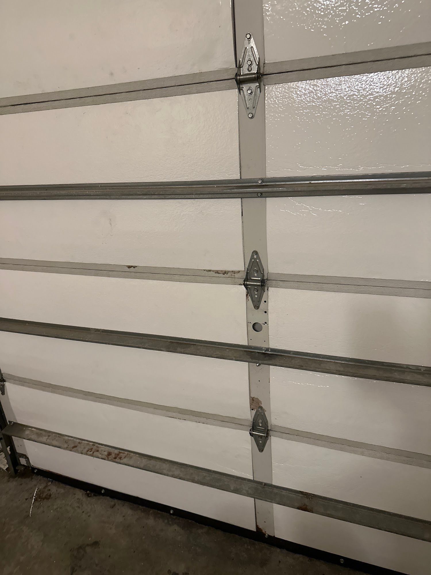 Closed white garage door with metal hinges and a dark floor at the bottom