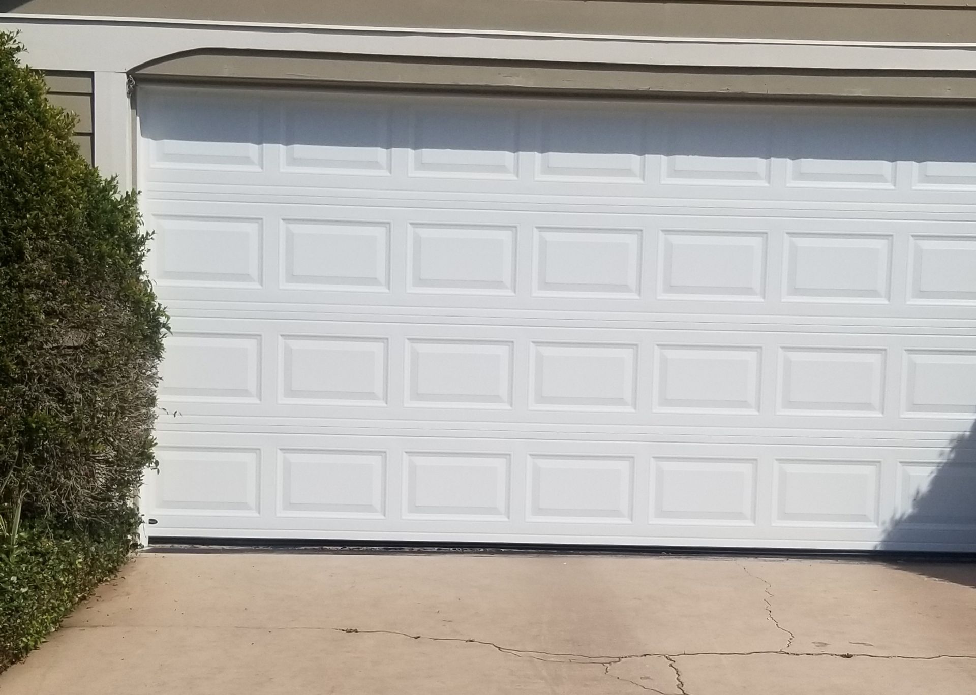 White garage door on a house with a concrete driveway and bushes on the left