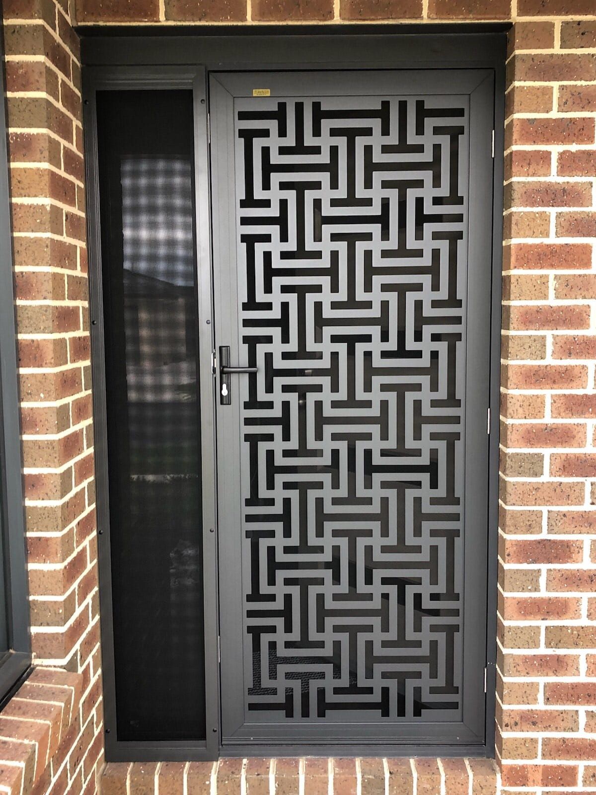 A black door with a maze pattern on it is on a brick wall.