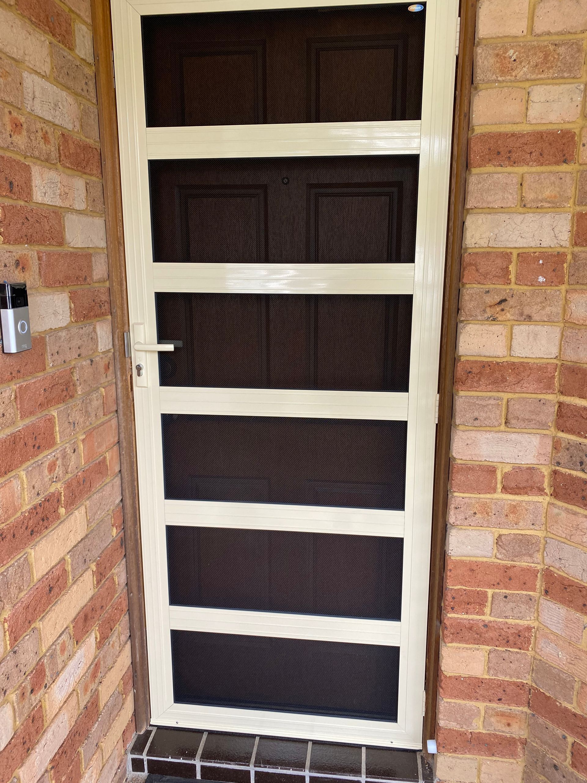 A white screen door is sitting on a brick wall.