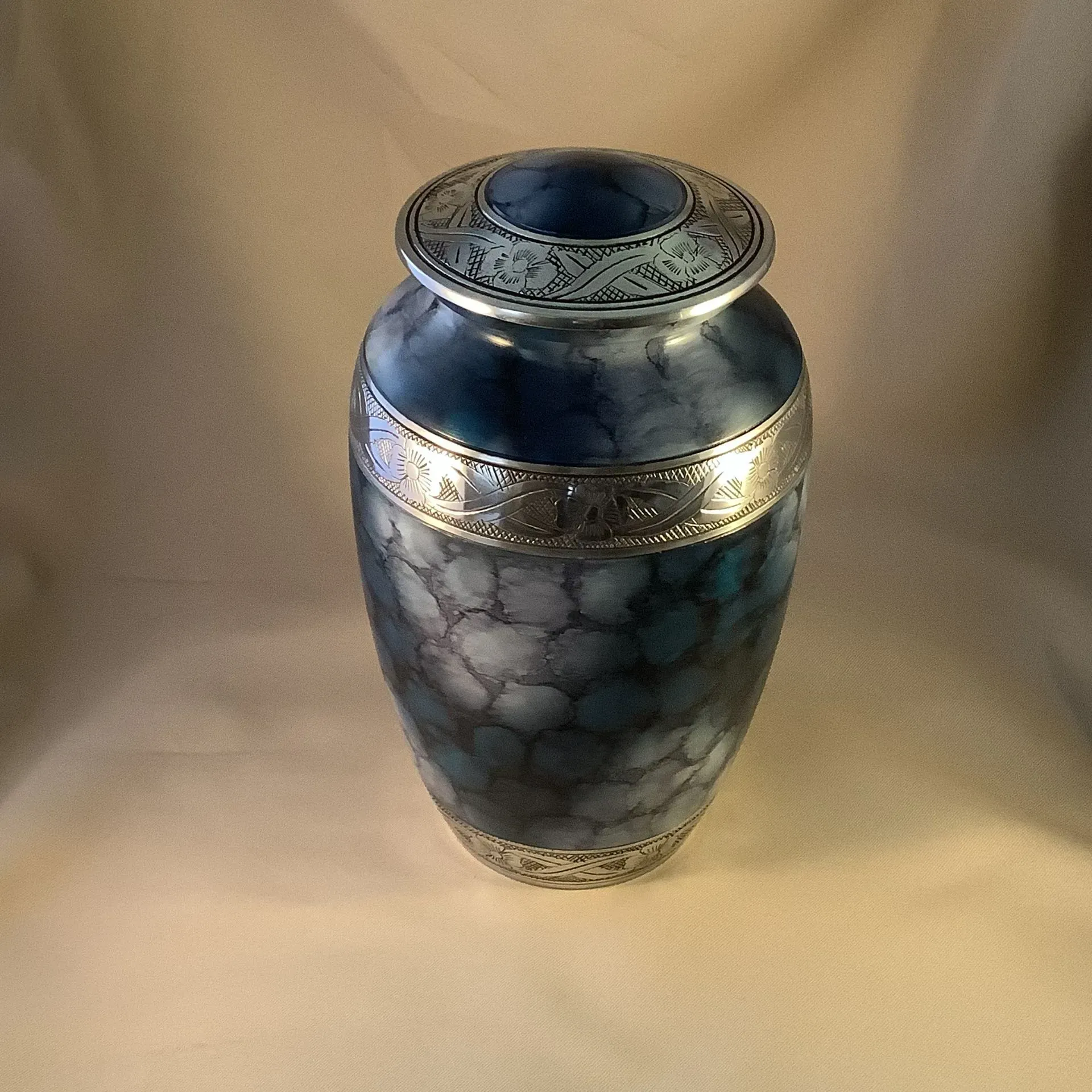 Blue ceramic vase with silver bands and a crackled glaze on a beige backdrop